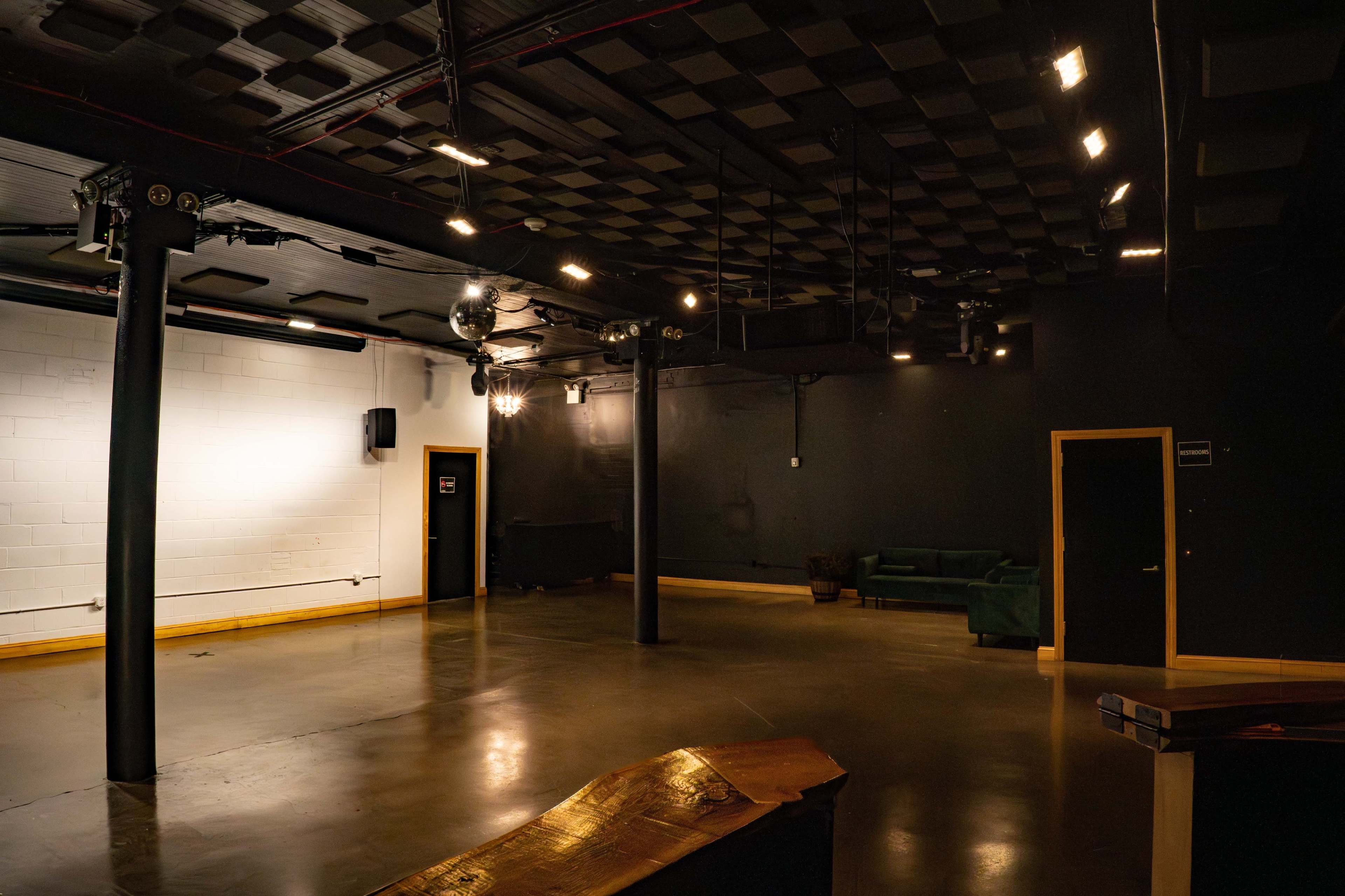 The image shows an empty, dimly lit room with polished concrete flooring, exposed ceiling beams, and a green couch along one wall.