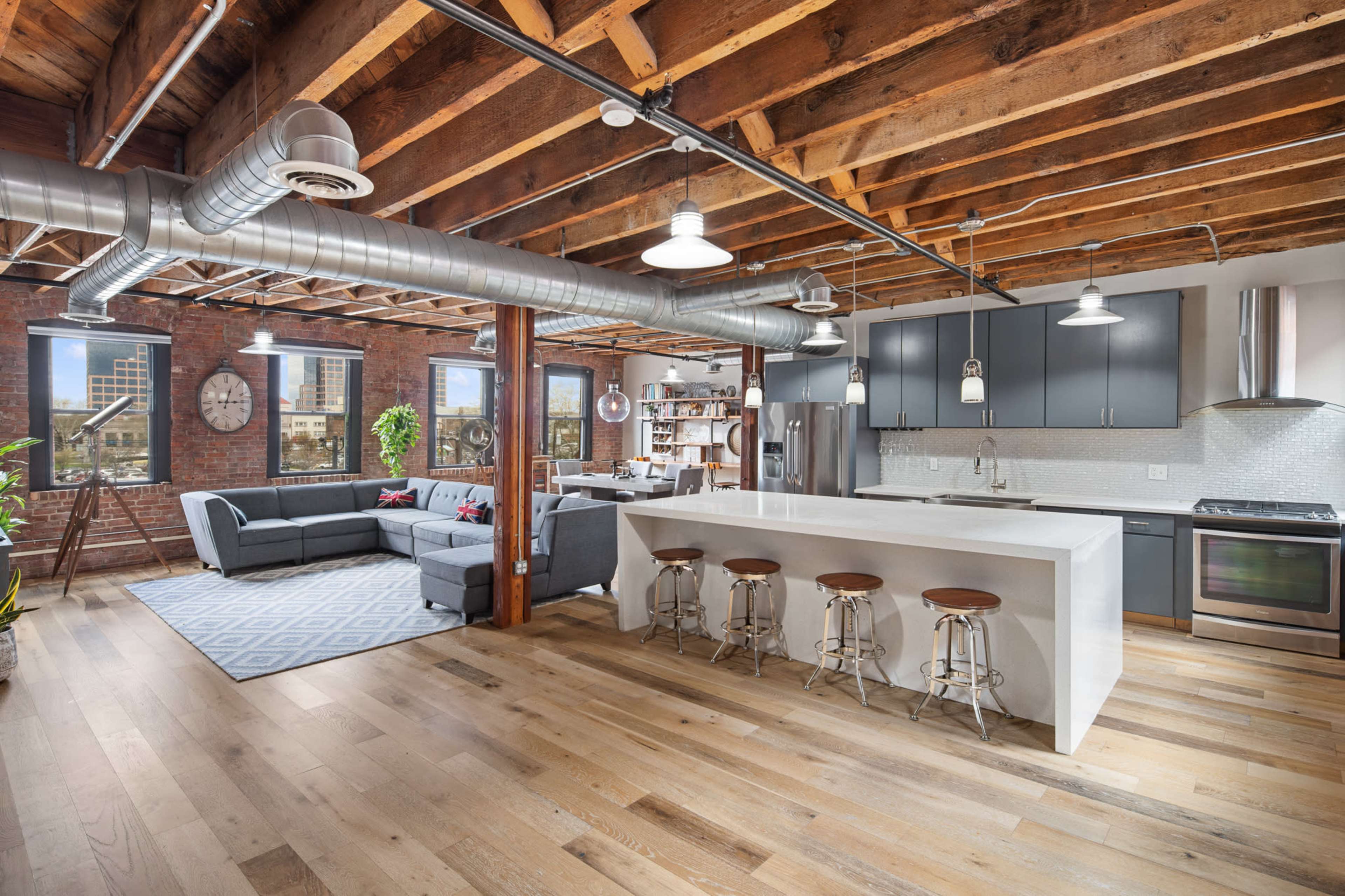 A modern open-concept kitchen and living area with exposed wooden beams, a large island with barstools, and a sectional sofa.
