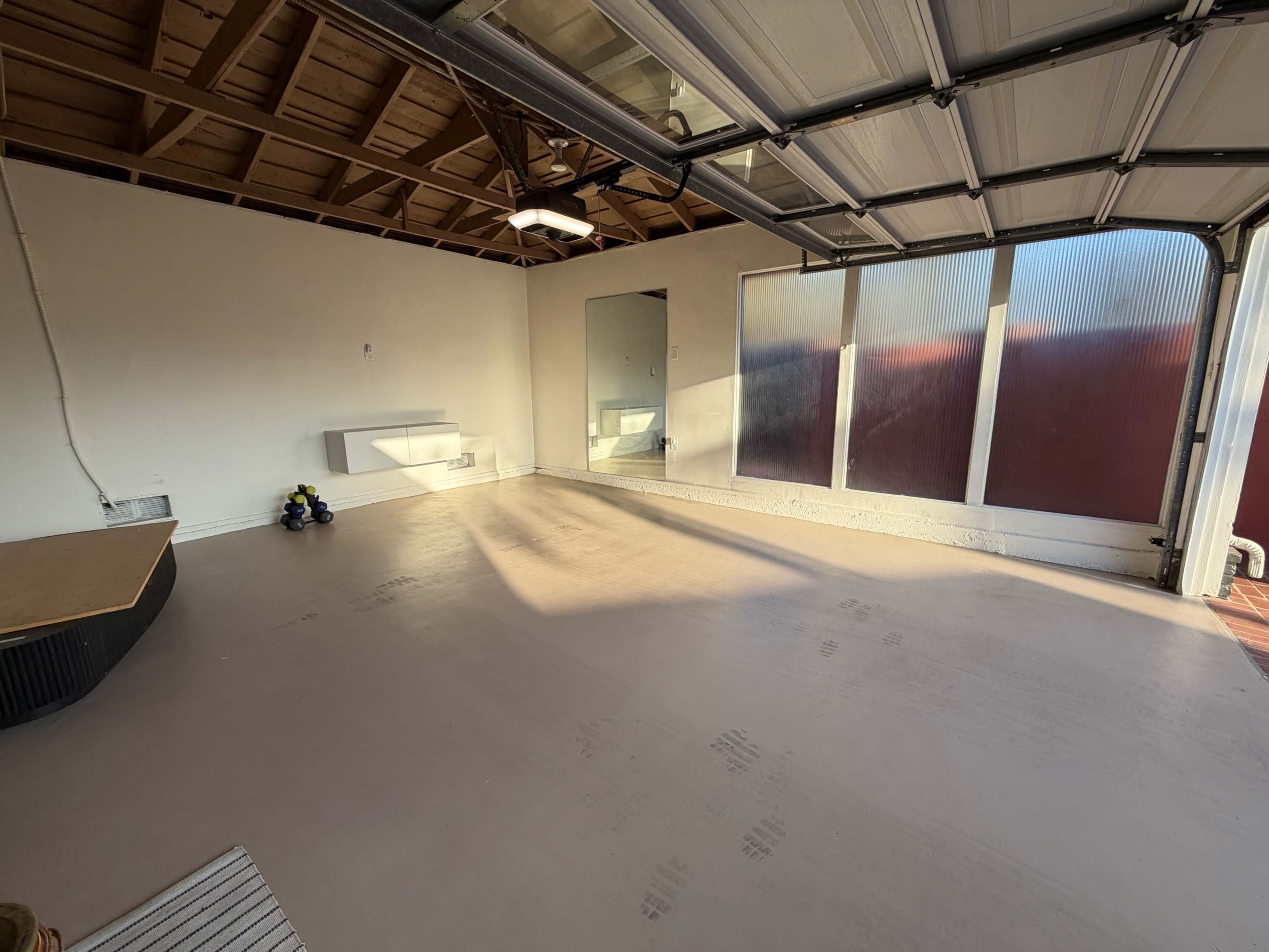 The image shows a spacious, empty garage with a concrete floor, a large garage door, and a mirror mounted on the wall.