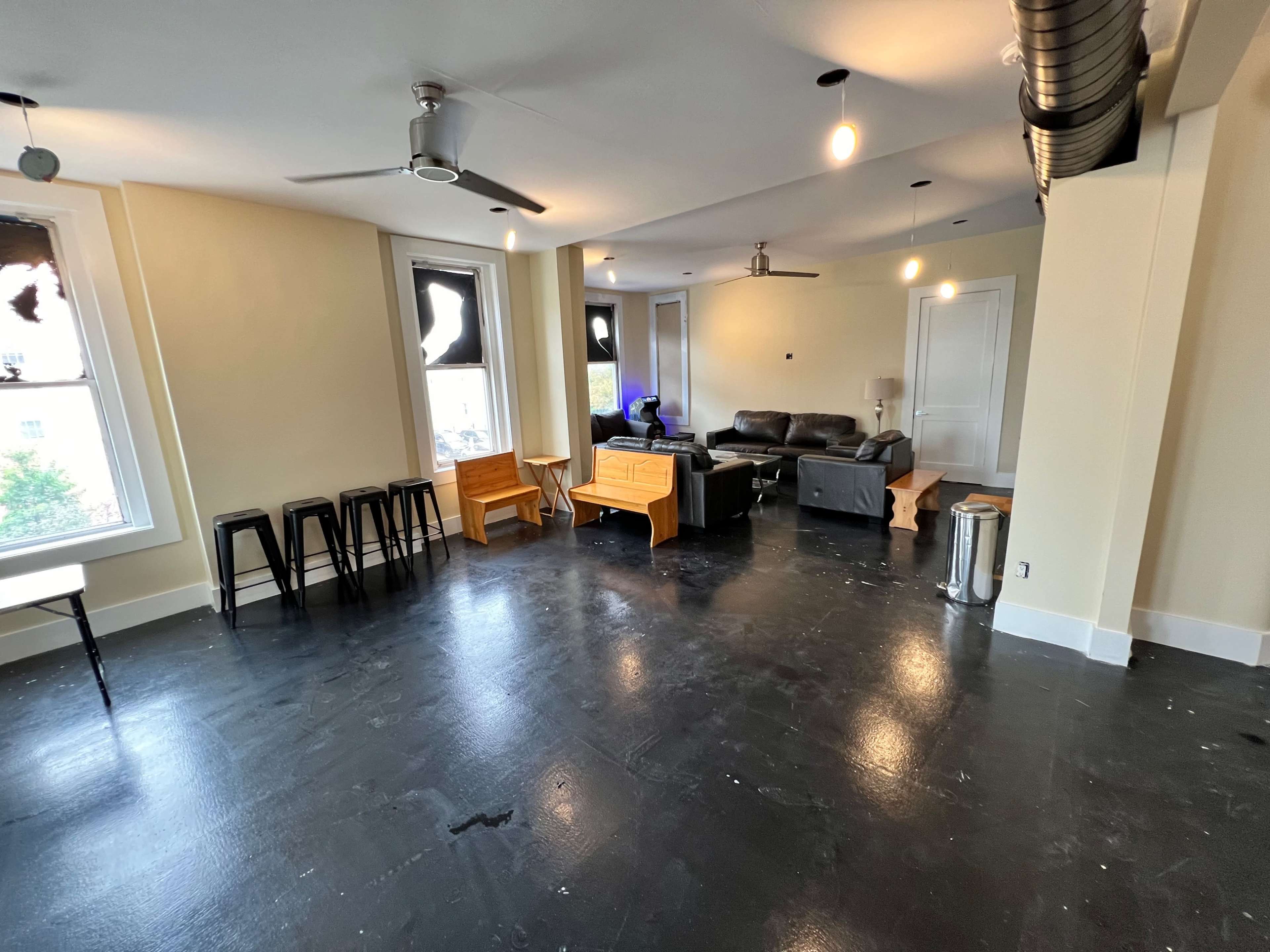 A spacious, unfurnished room with black flooring, featuring a seating area with a black couch and two ceiling fans.