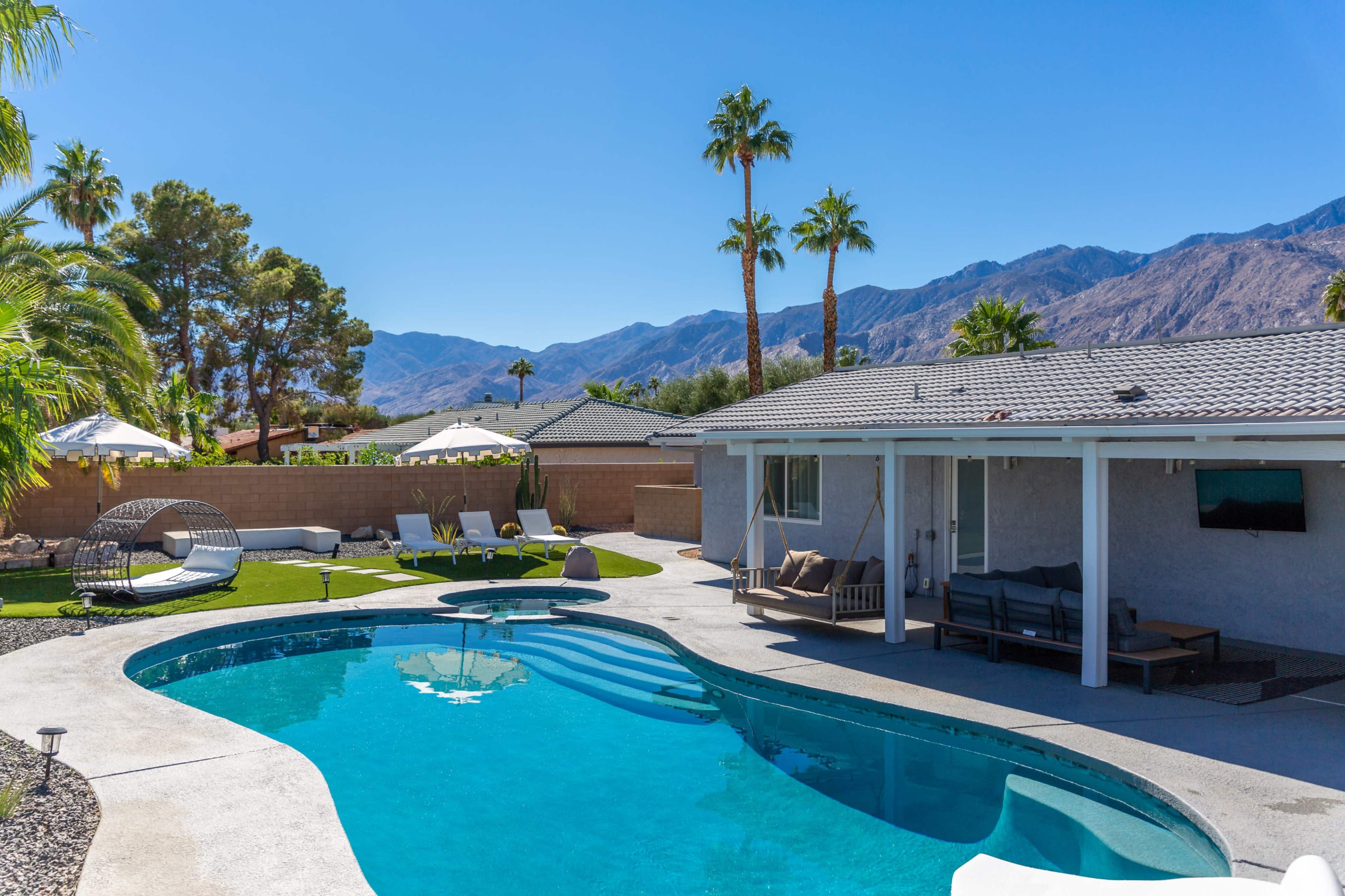 The image shows a backyard pool area surrounded by palm trees, lounge chairs, and a view of mountains in the background.