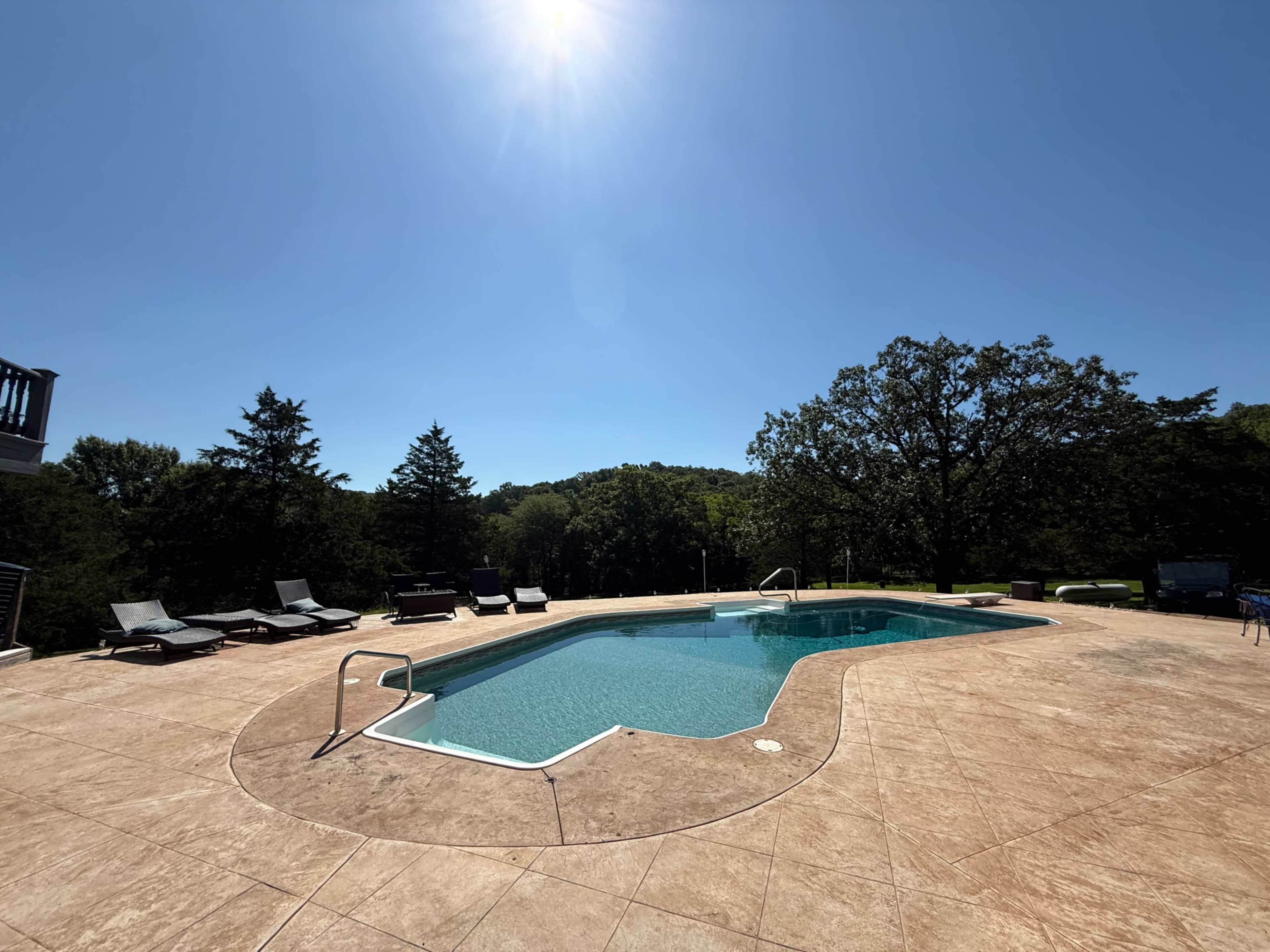 A clear blue sky overlooks a swimming pool surrounded by lounge chairs and greenery.