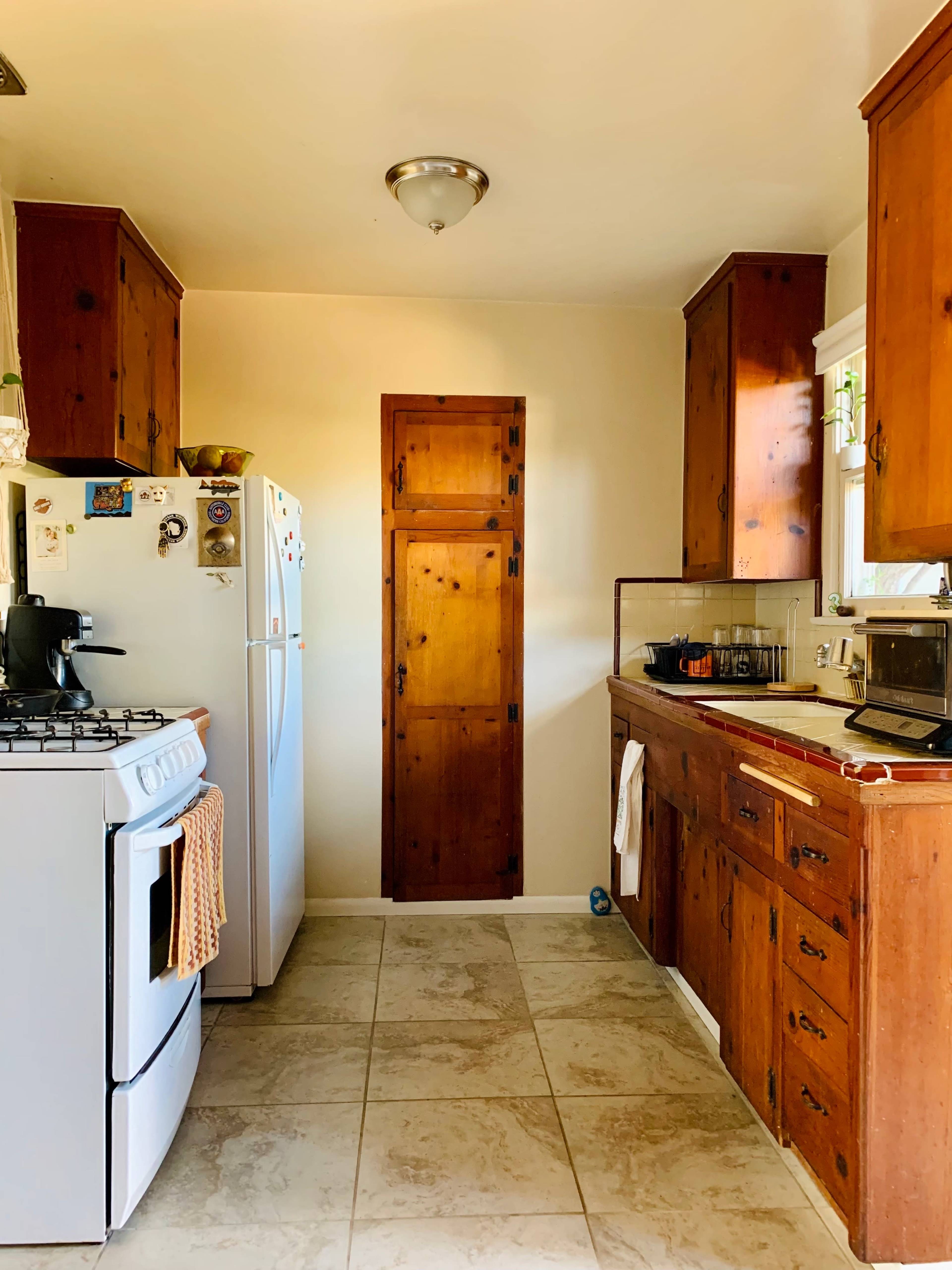 A kitchen with wooden cabinets, a white refrigerator, a gas stove, and a door leading to another room.