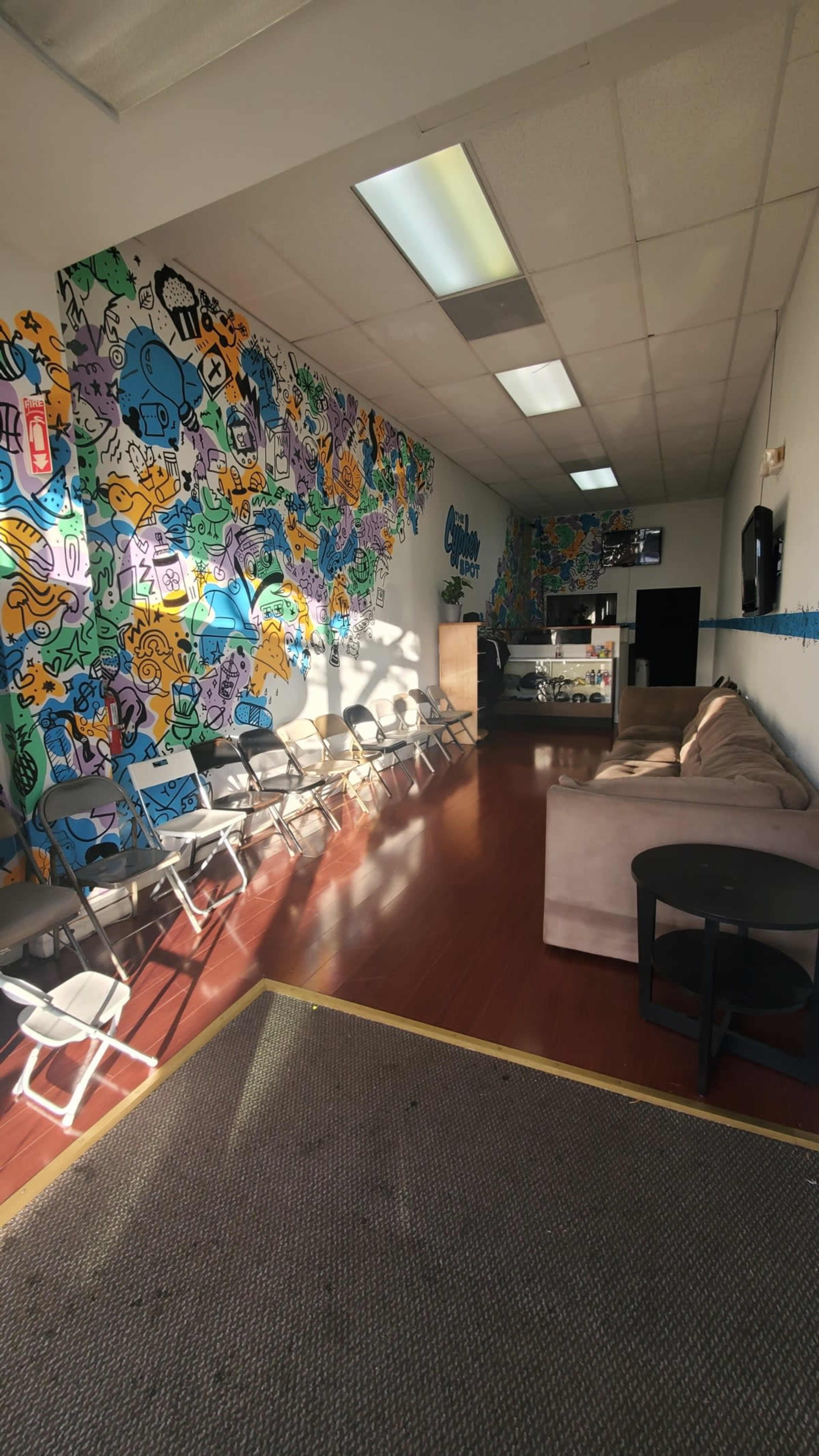 An indoor room with vibrant, mural-covered walls, a seating area with metal chairs, and a couch near a front counter.