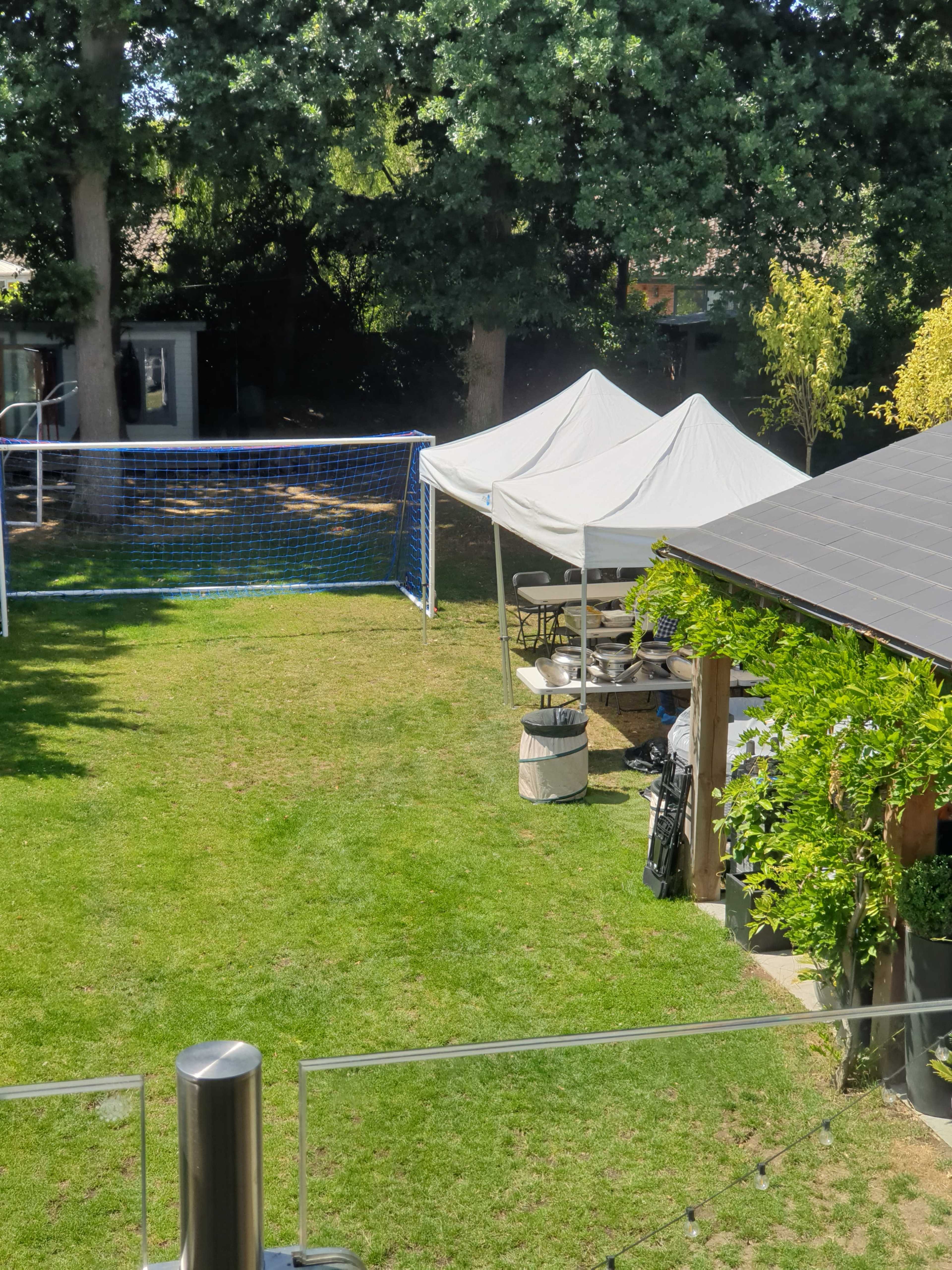 A backyard with a soccer goal, a tent, and a seating area surrounded by trees.