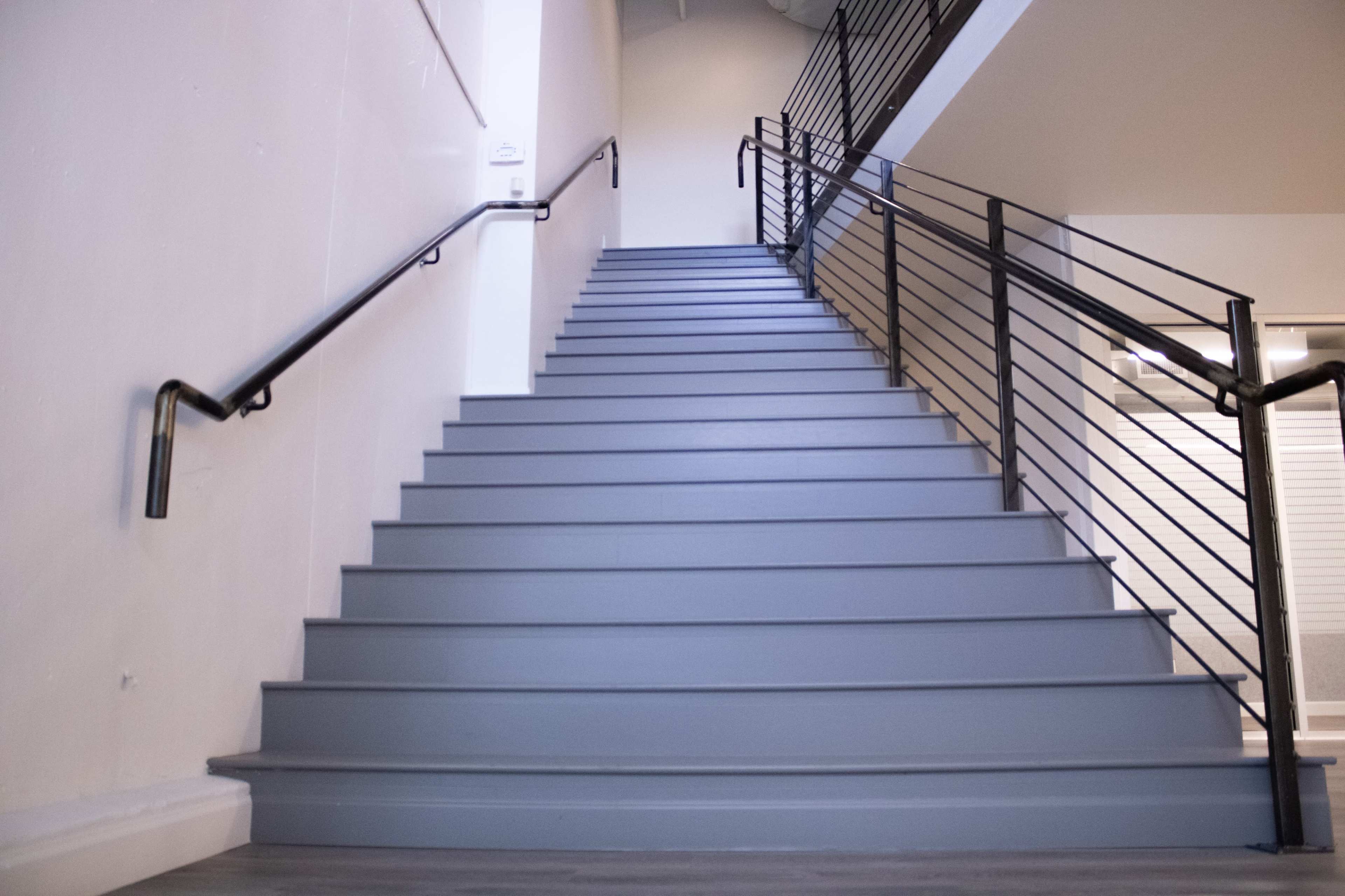 The image shows a set of gray stairs leading upward, flanked by a metal railing on one side.