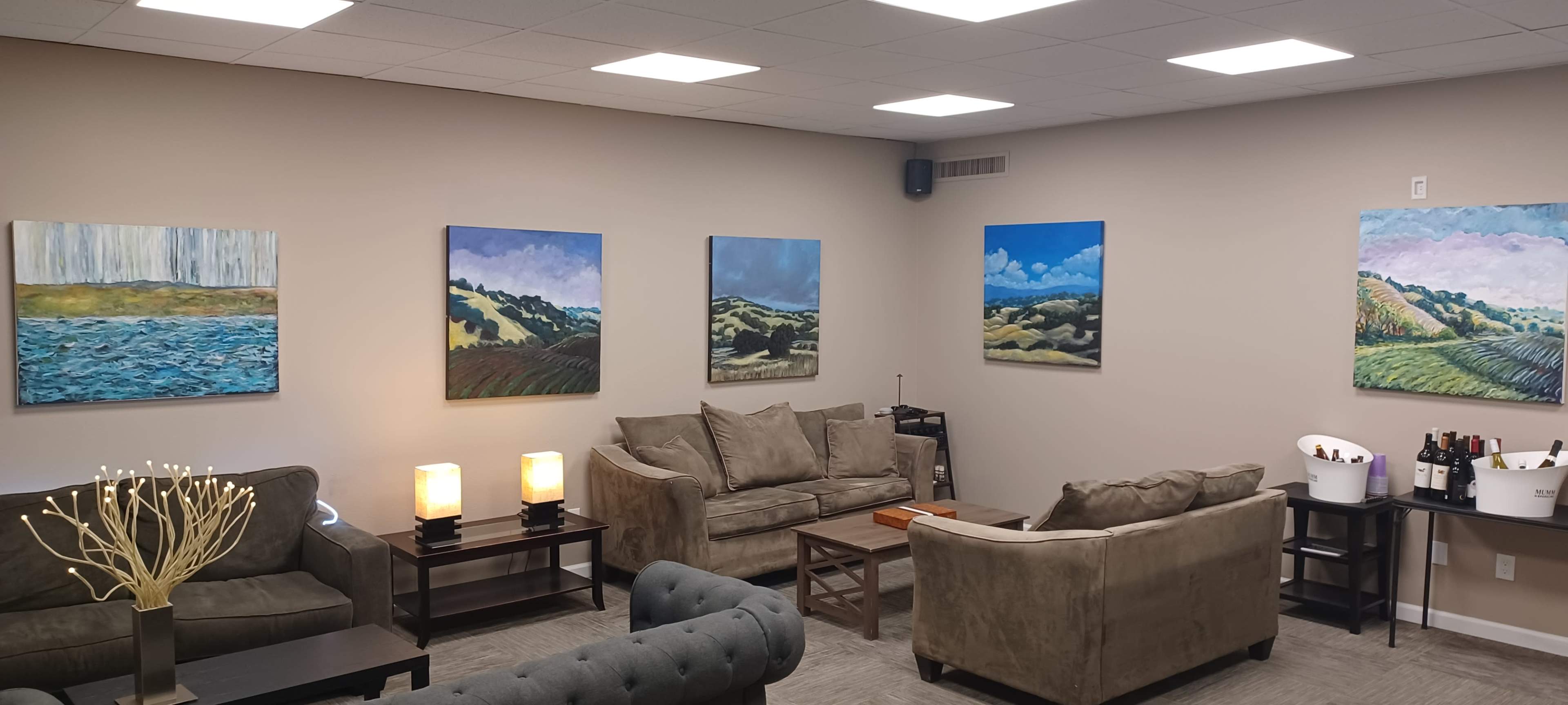 The image shows a lounge area with two sofas, a coffee table, and several landscape paintings on the walls.