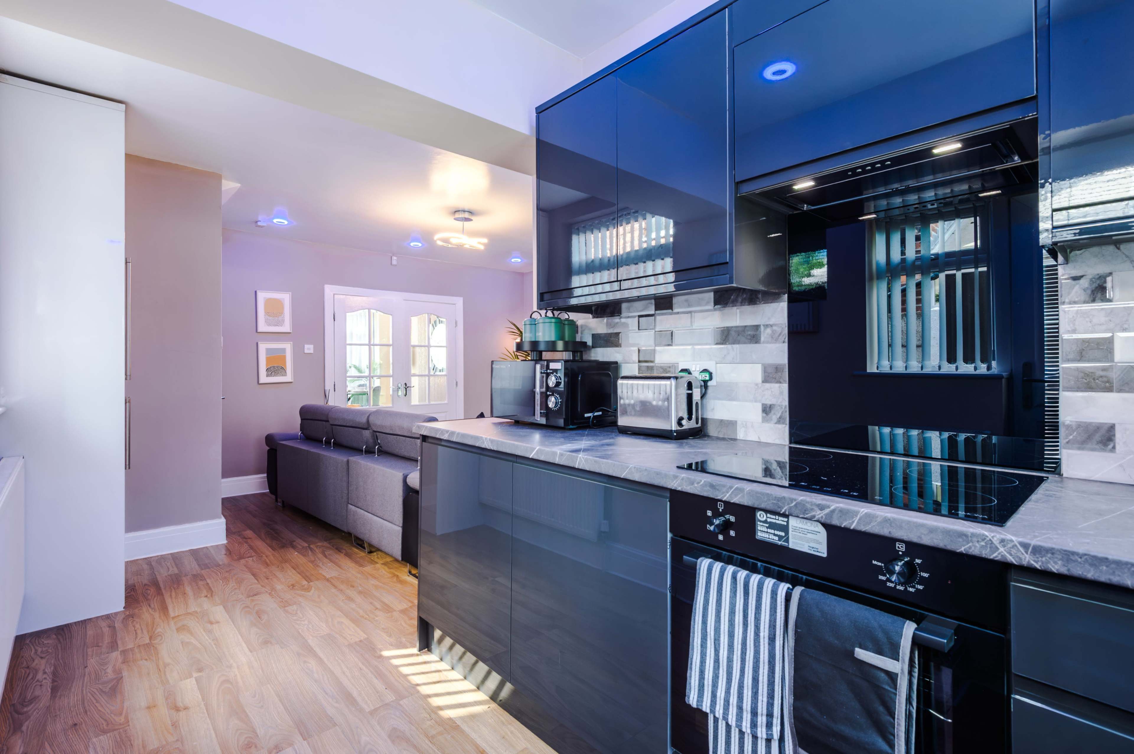 The image shows a modern kitchen featuring dark blue cabinets, a sleek stove, and a living area visible in the background.