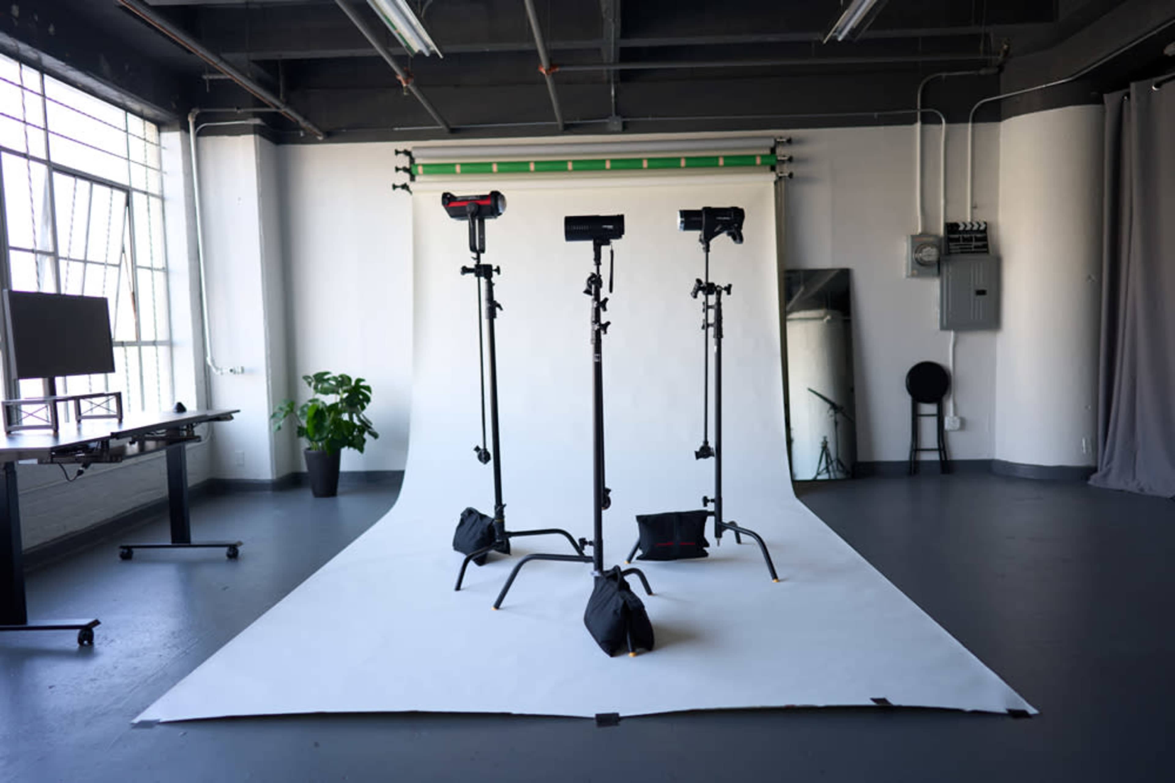 A photography studio with three light stands positioned on a white backdrop, alongside a black table and a potted plant.