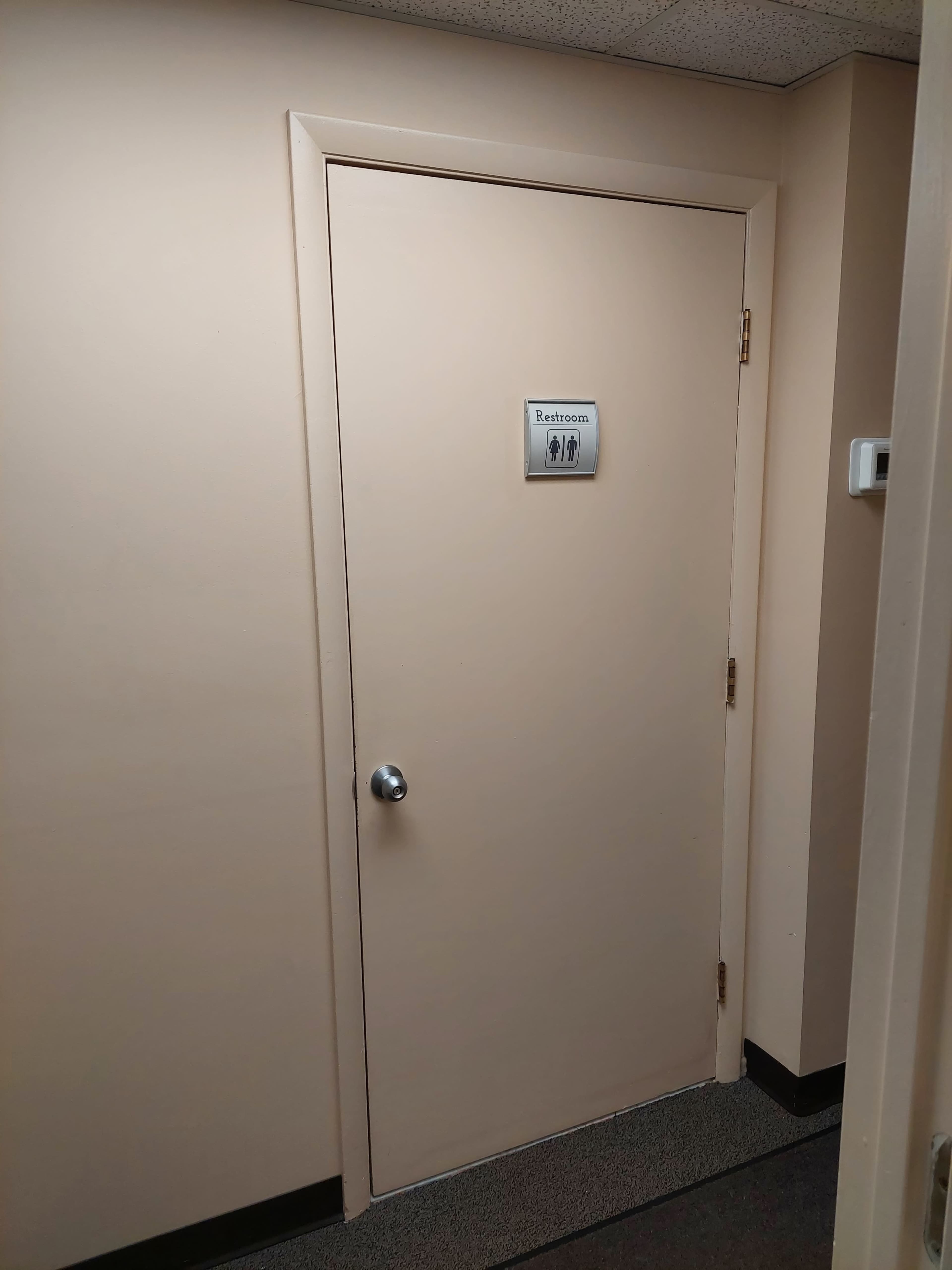 A beige door labeled "Restroom" is situated in a hallway with a plain, light-colored wall.
