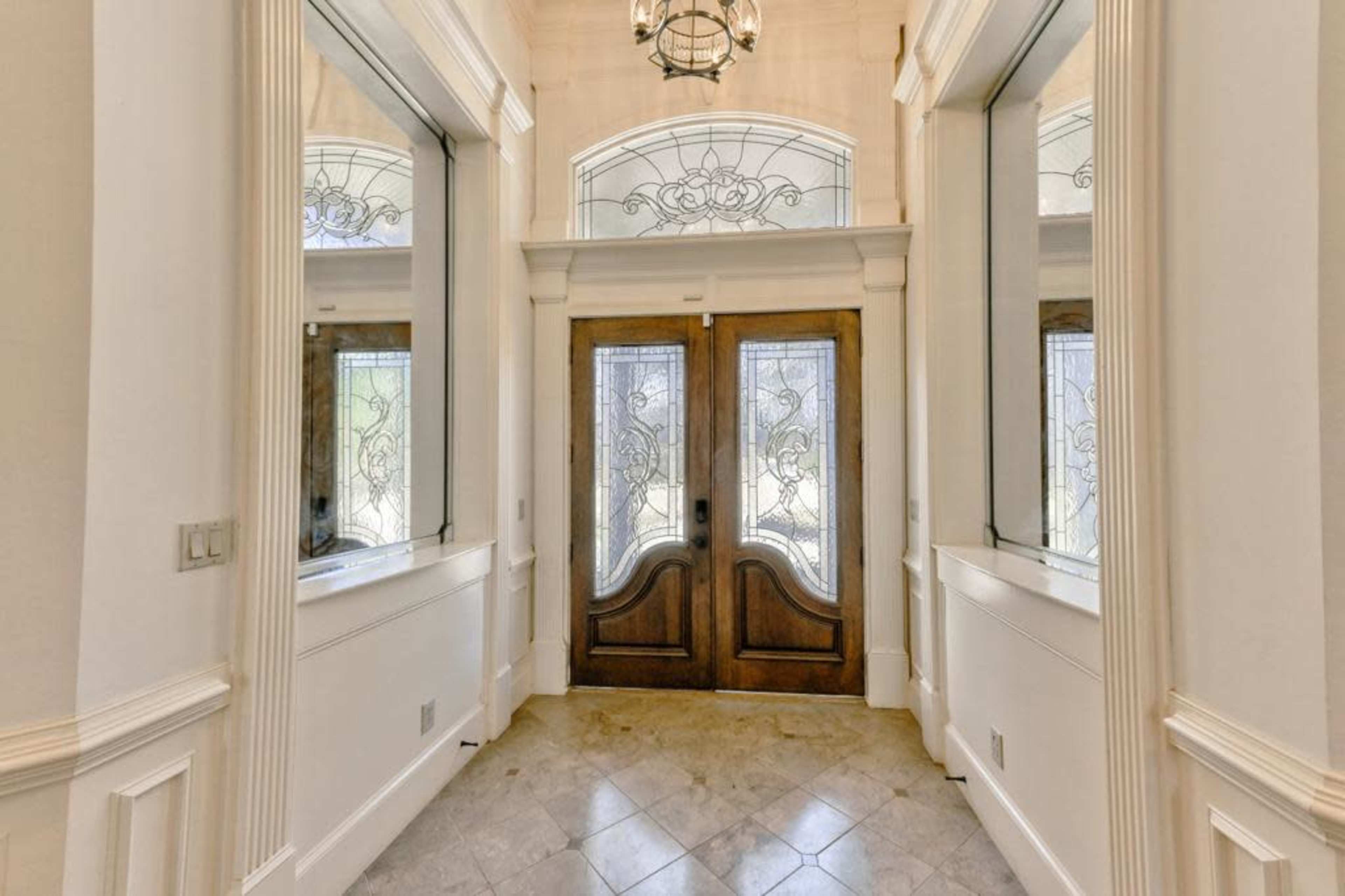 A spacious entryway with double wooden doors and large windows on either side.