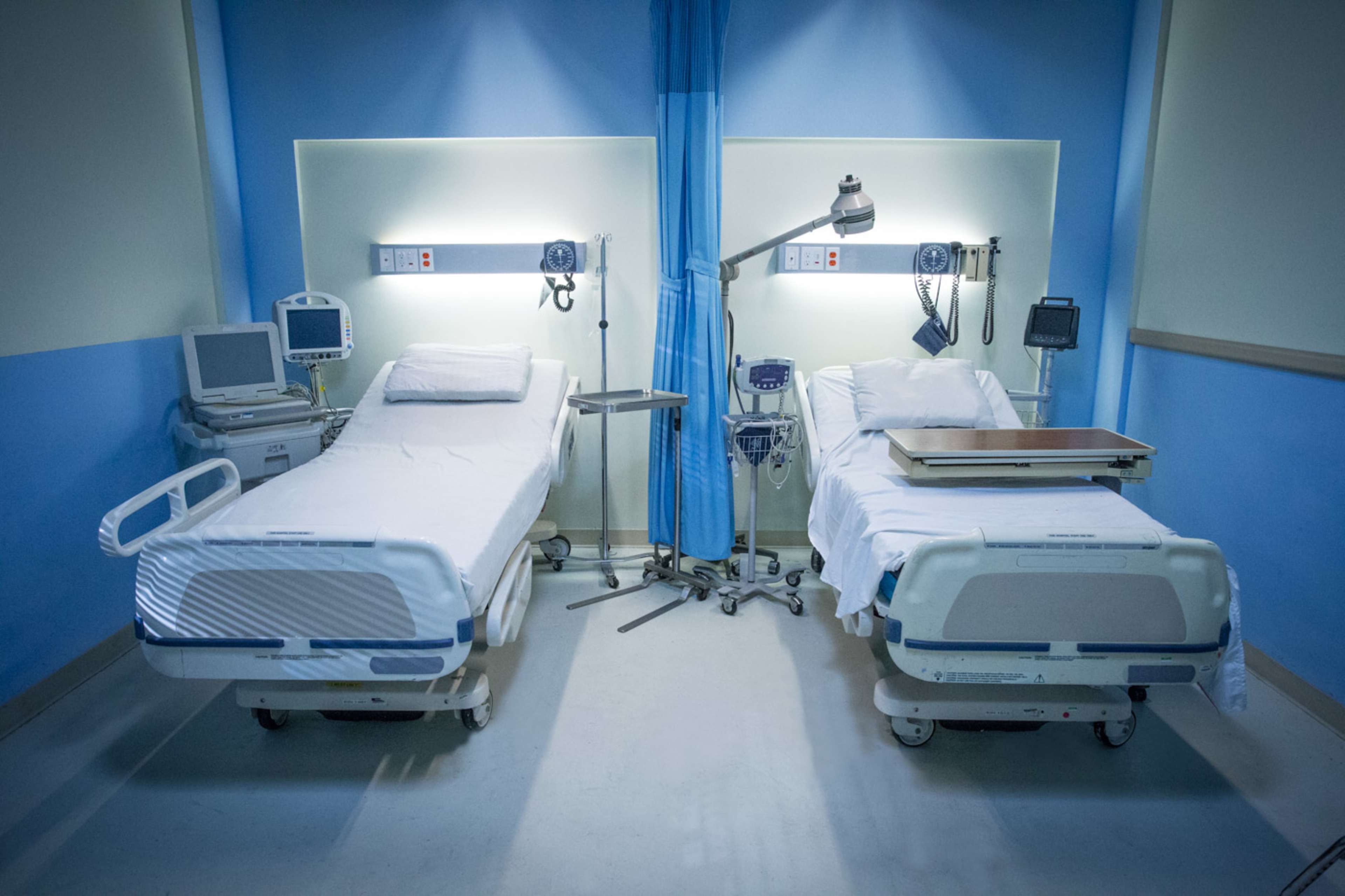 A hospital room with two unoccupied beds, medical equipment, and a blue and white color scheme.