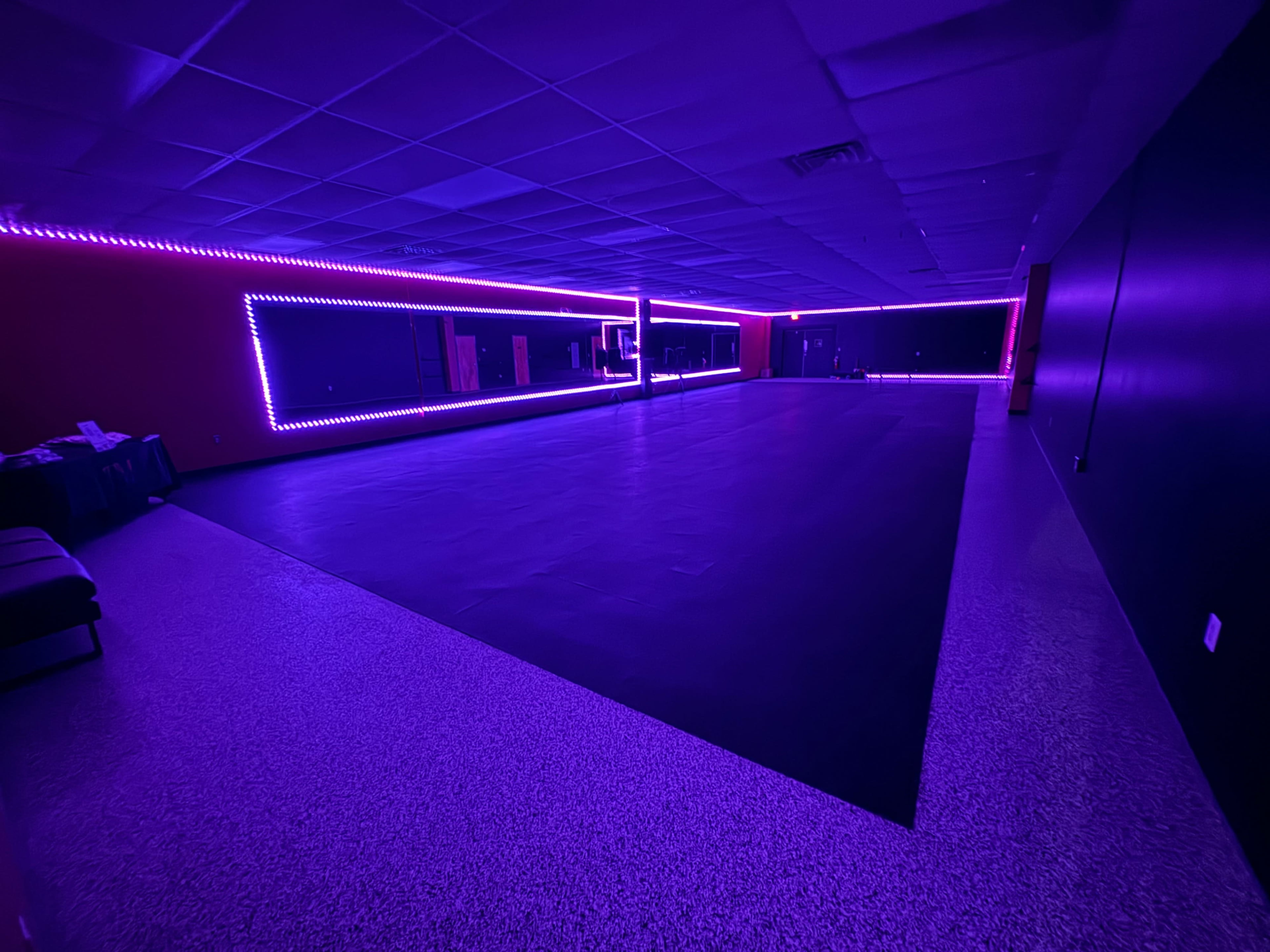 A dimly lit dance studio with purple LED lights highlighting the walls and mirrors.