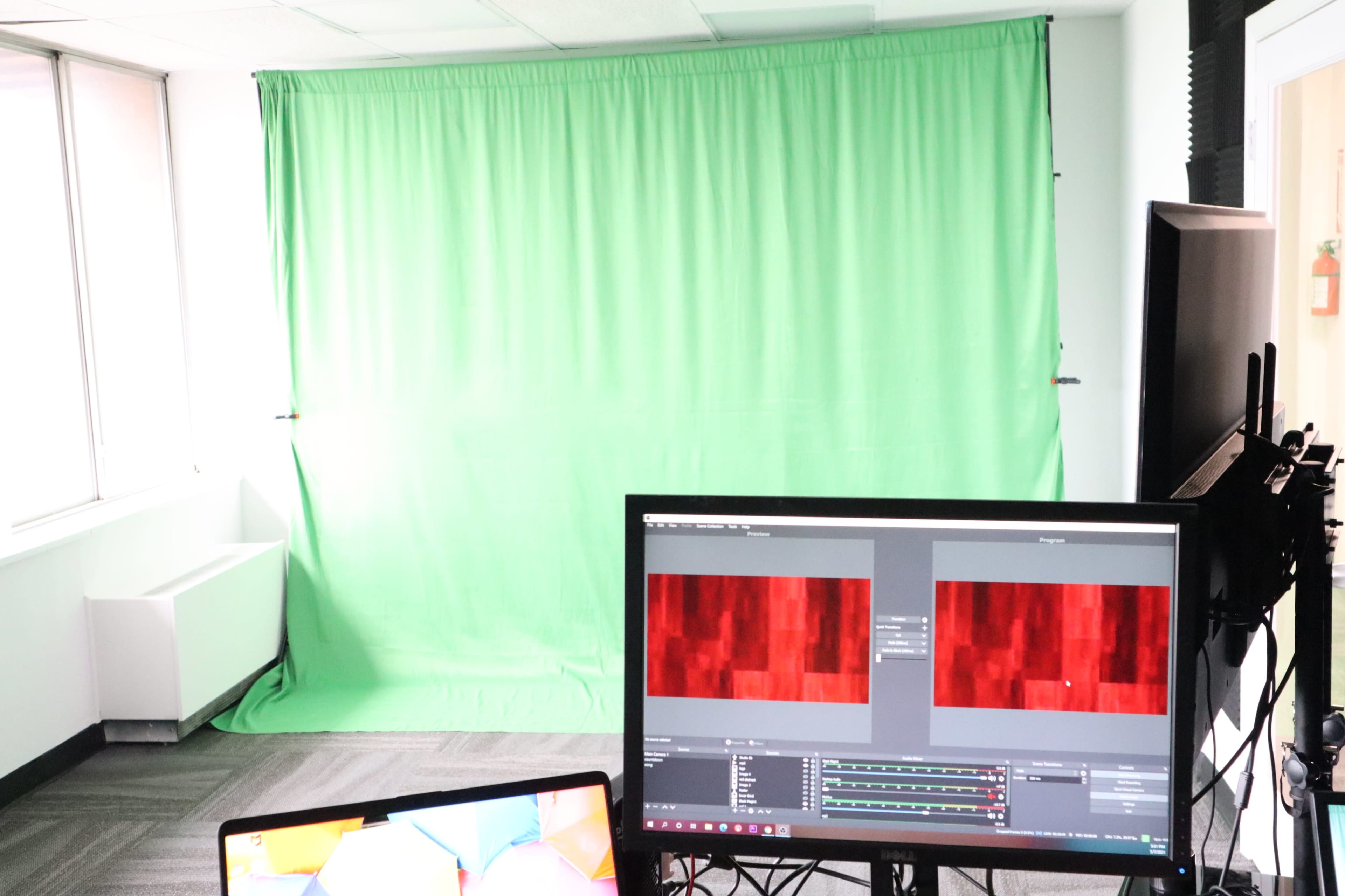 A studio setup with a green screen backdrop and two computer monitors displaying abstract patterns.