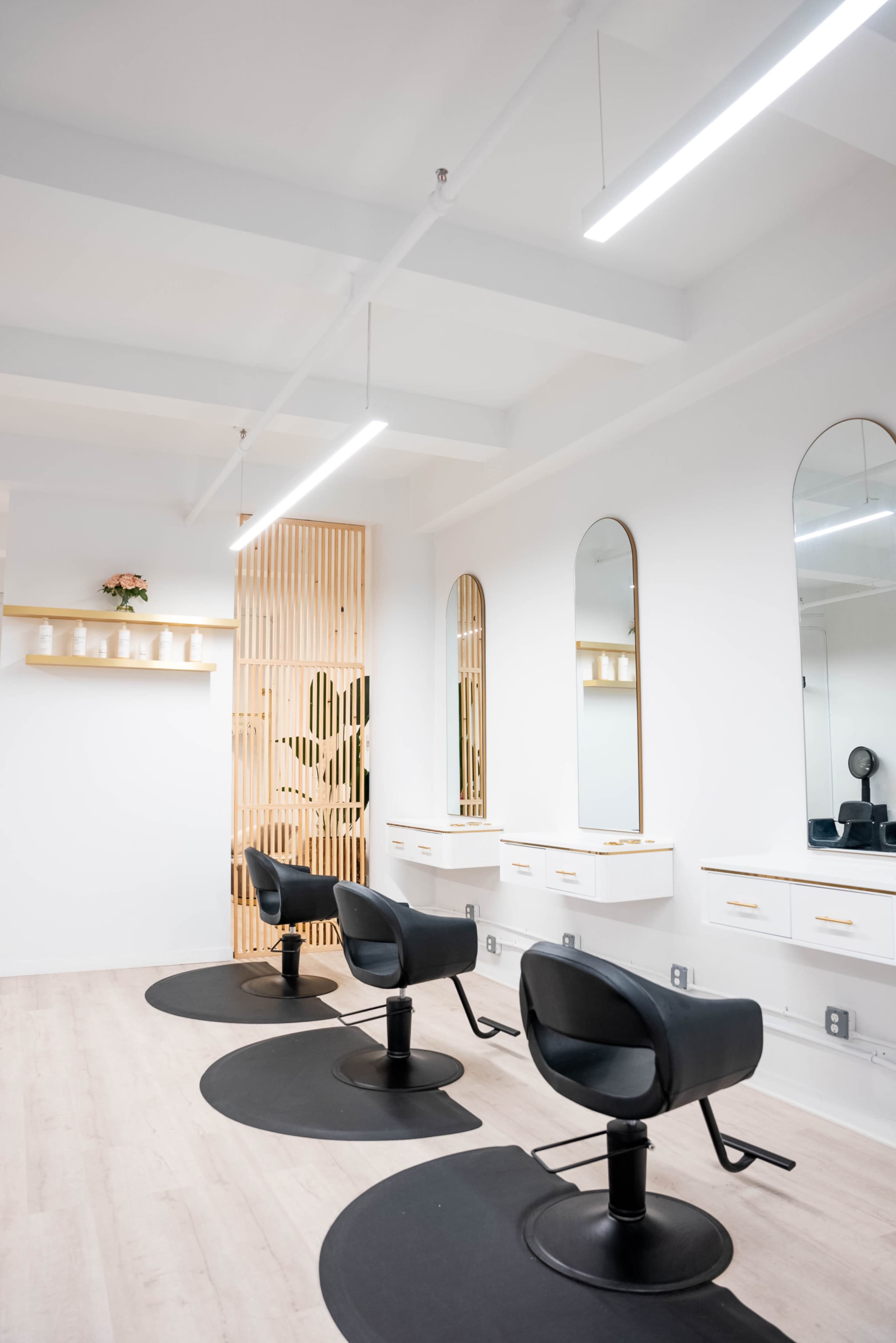 A stylish hair salon interior with three black salon chairs, large mirrors, and wooden accents.