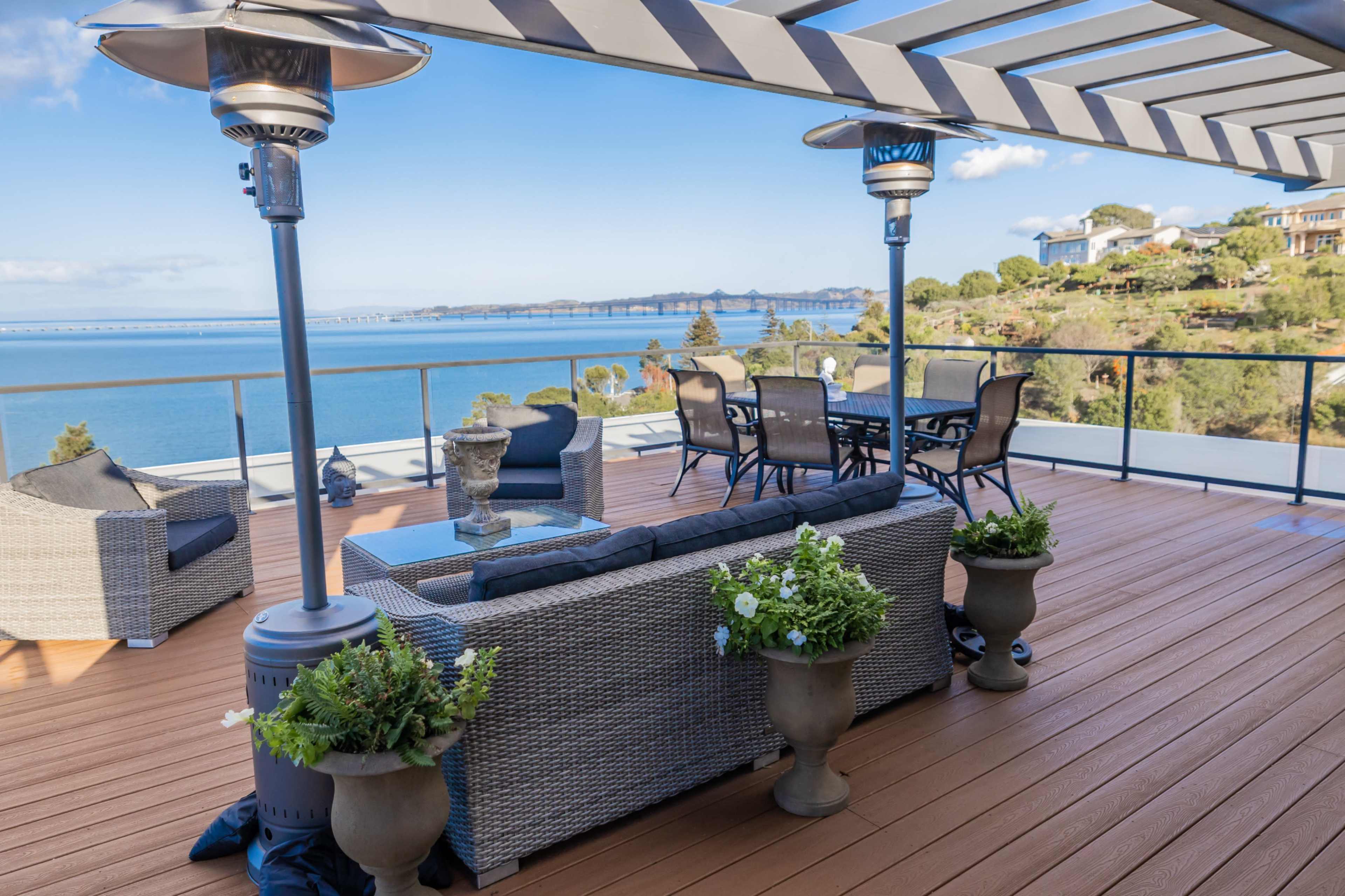 A spacious deck with outdoor furniture overlooking a body of water and a distant bridge.