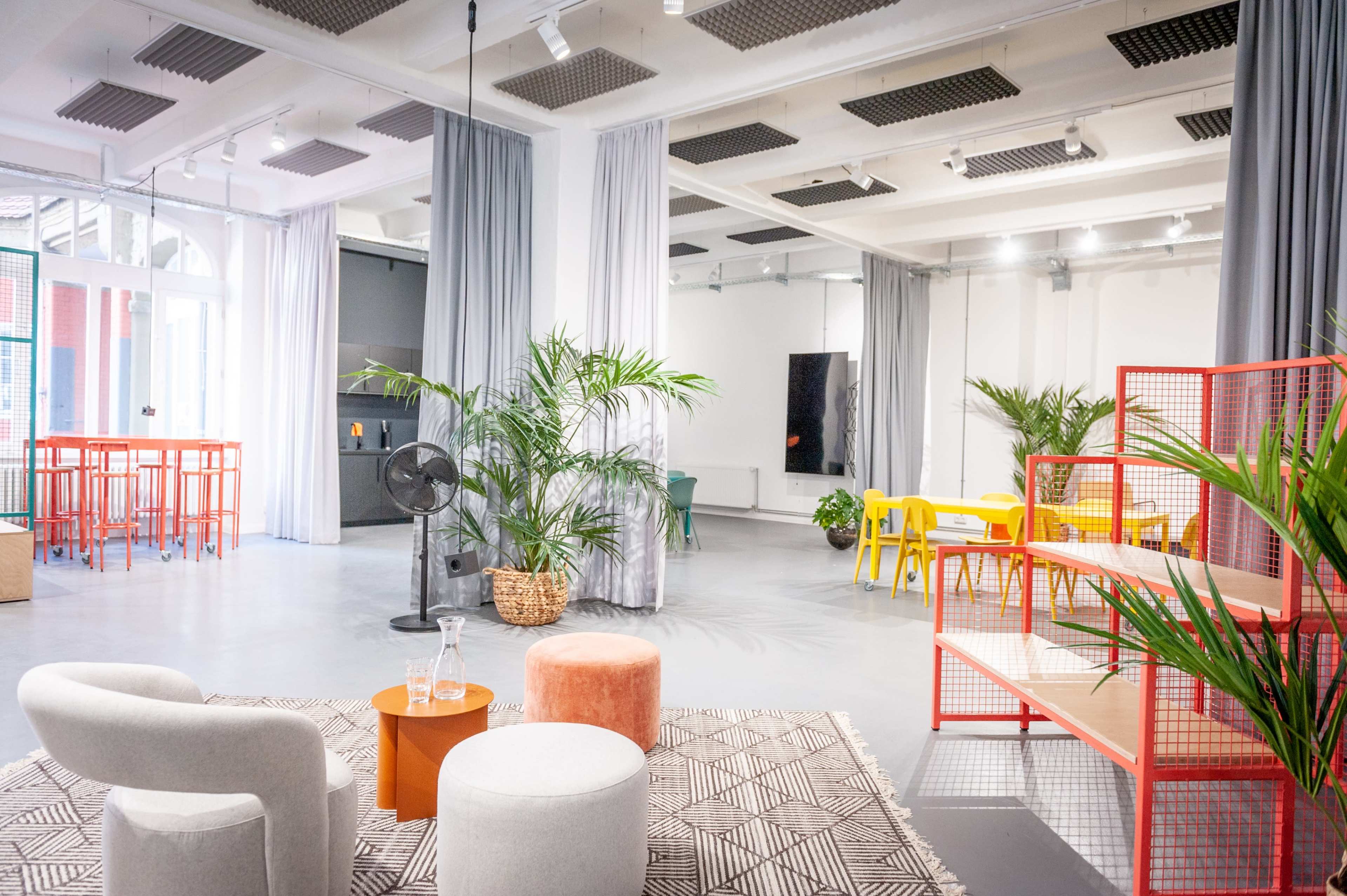 A modern, open space with various seating options, a bar area, and indoor plants arranged around a light-colored floor.