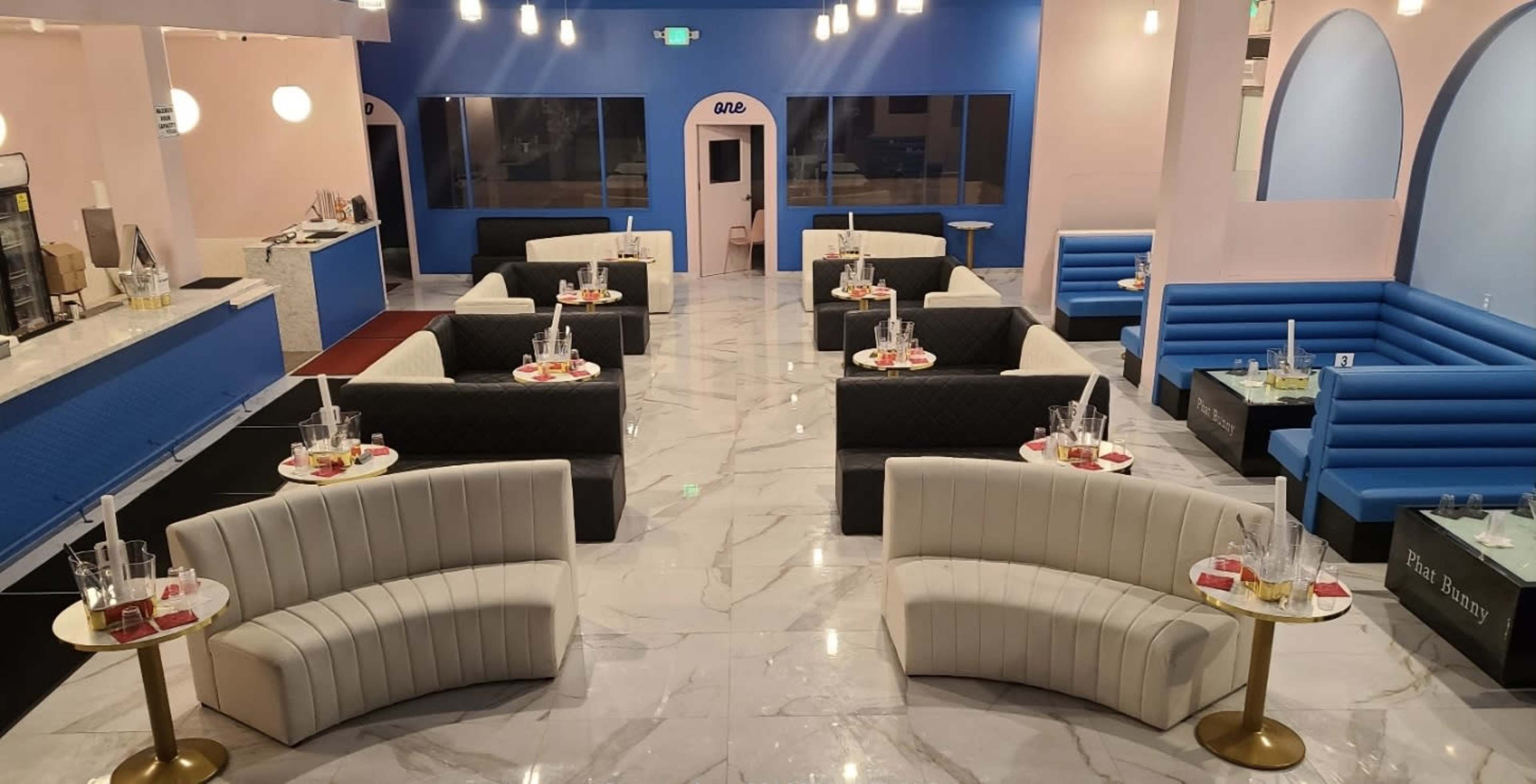 A modern lounge area with curved seating arrangements, marble flooring, and a bright color scheme featuring blue and pink walls.