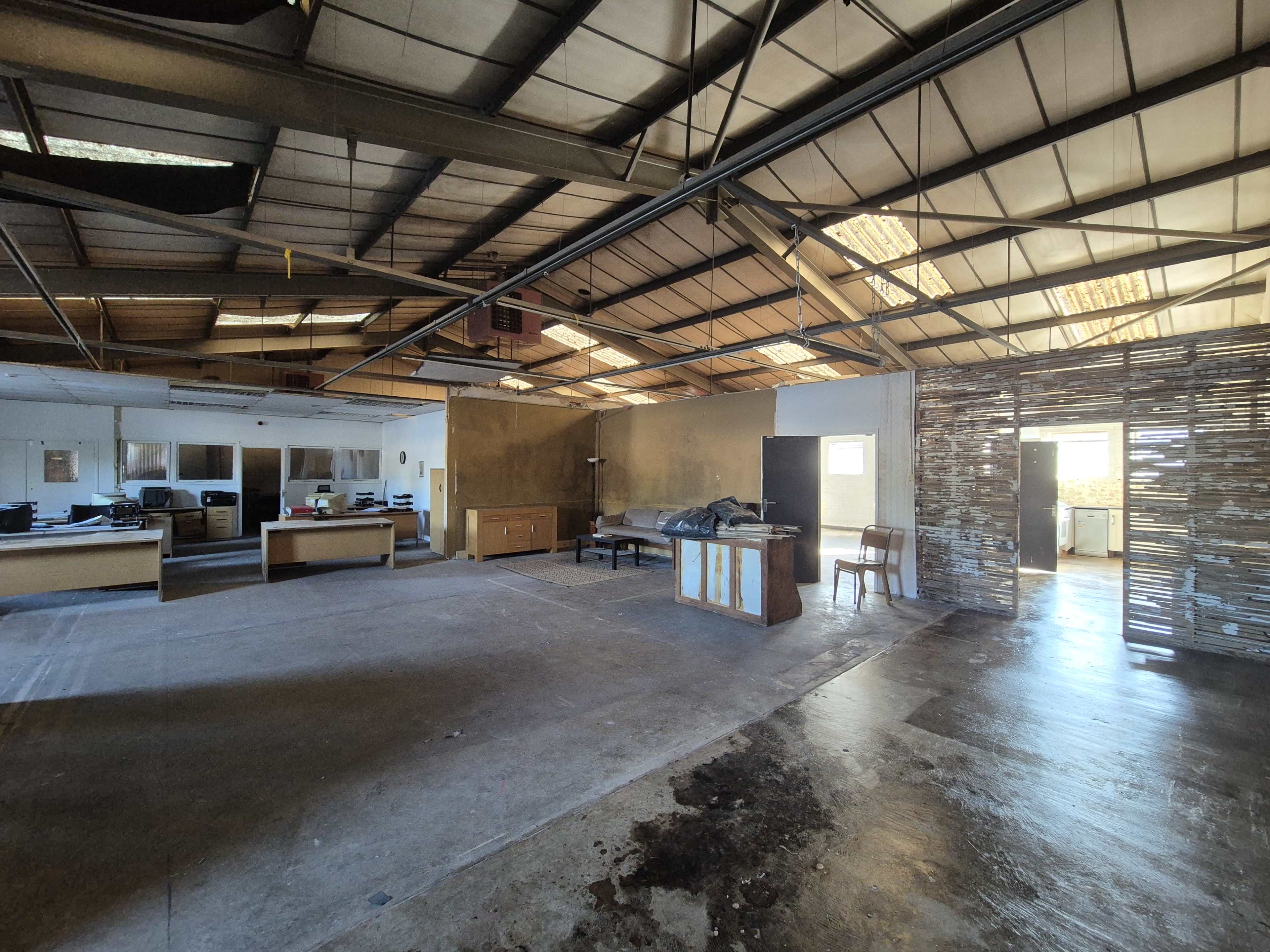 The image shows an empty industrial-style interior space with open areas, scattered furniture, and a partition made of wooden slats.
