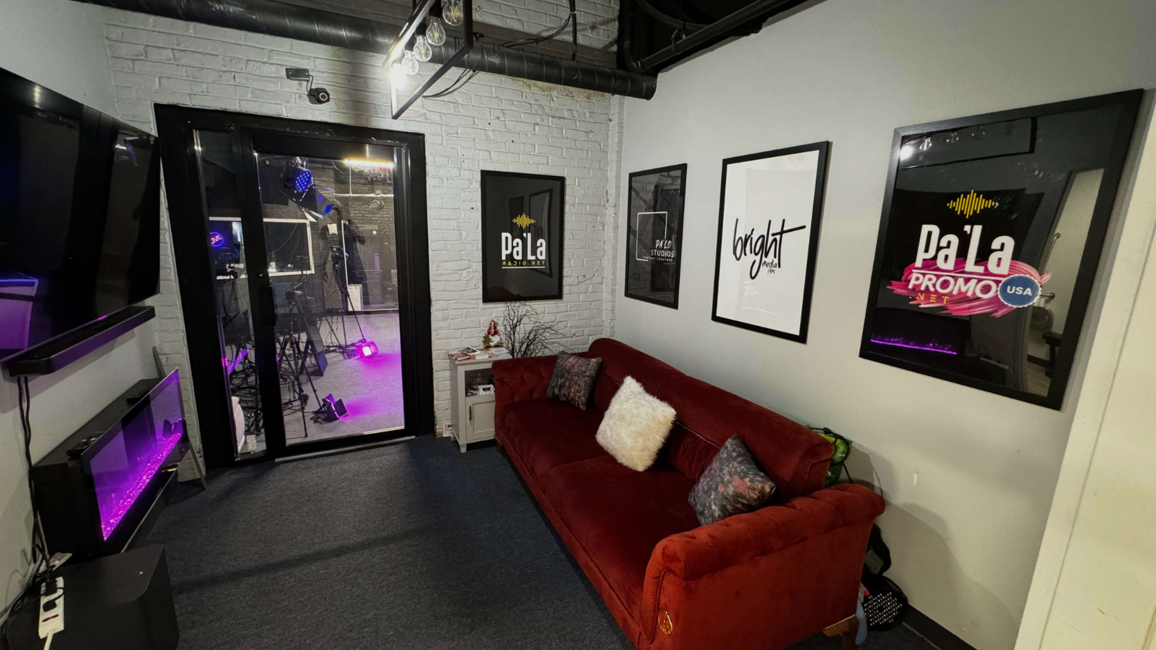 A small lounge area with a red sofa, framed artwork on the walls, and a glass door leading to a room with purple lighting.