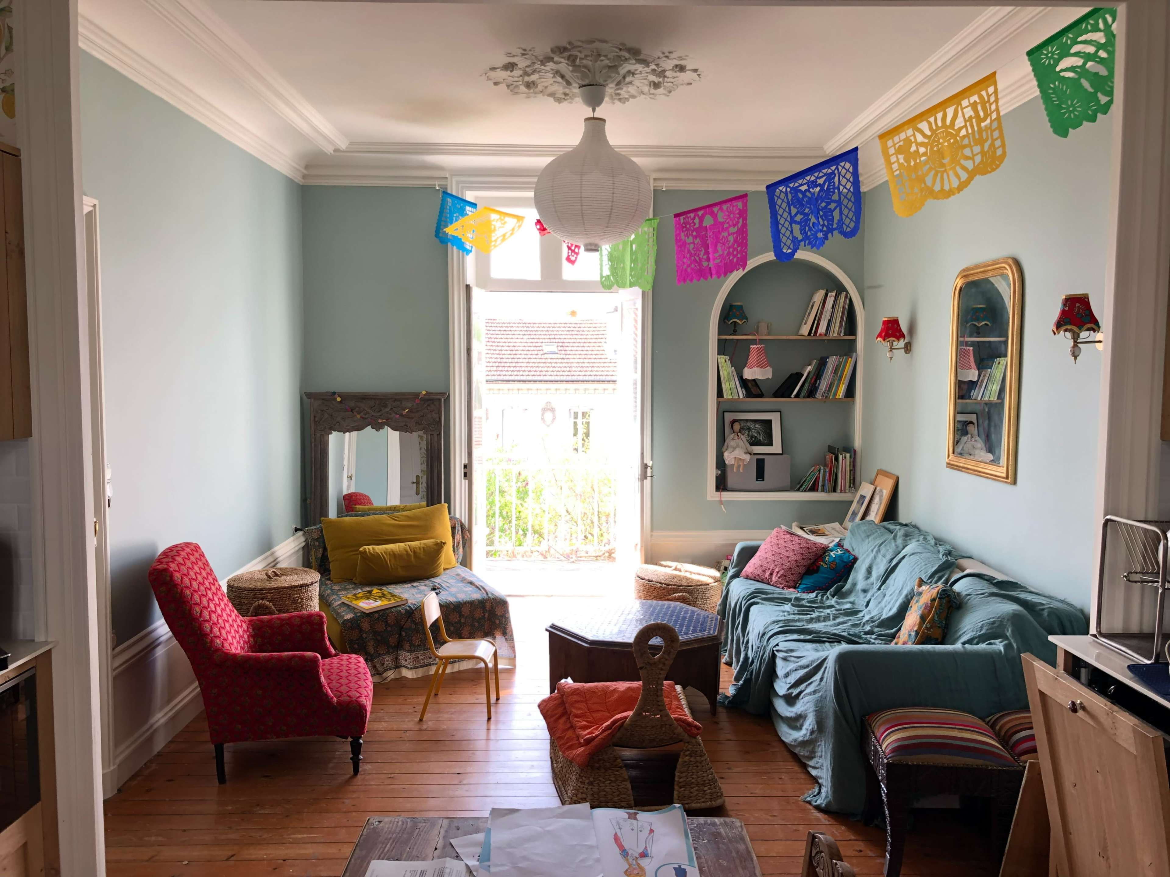 A cozy living room features a blue sofa, patterned chairs, and colorful papel picado decorations hanging from the ceiling.