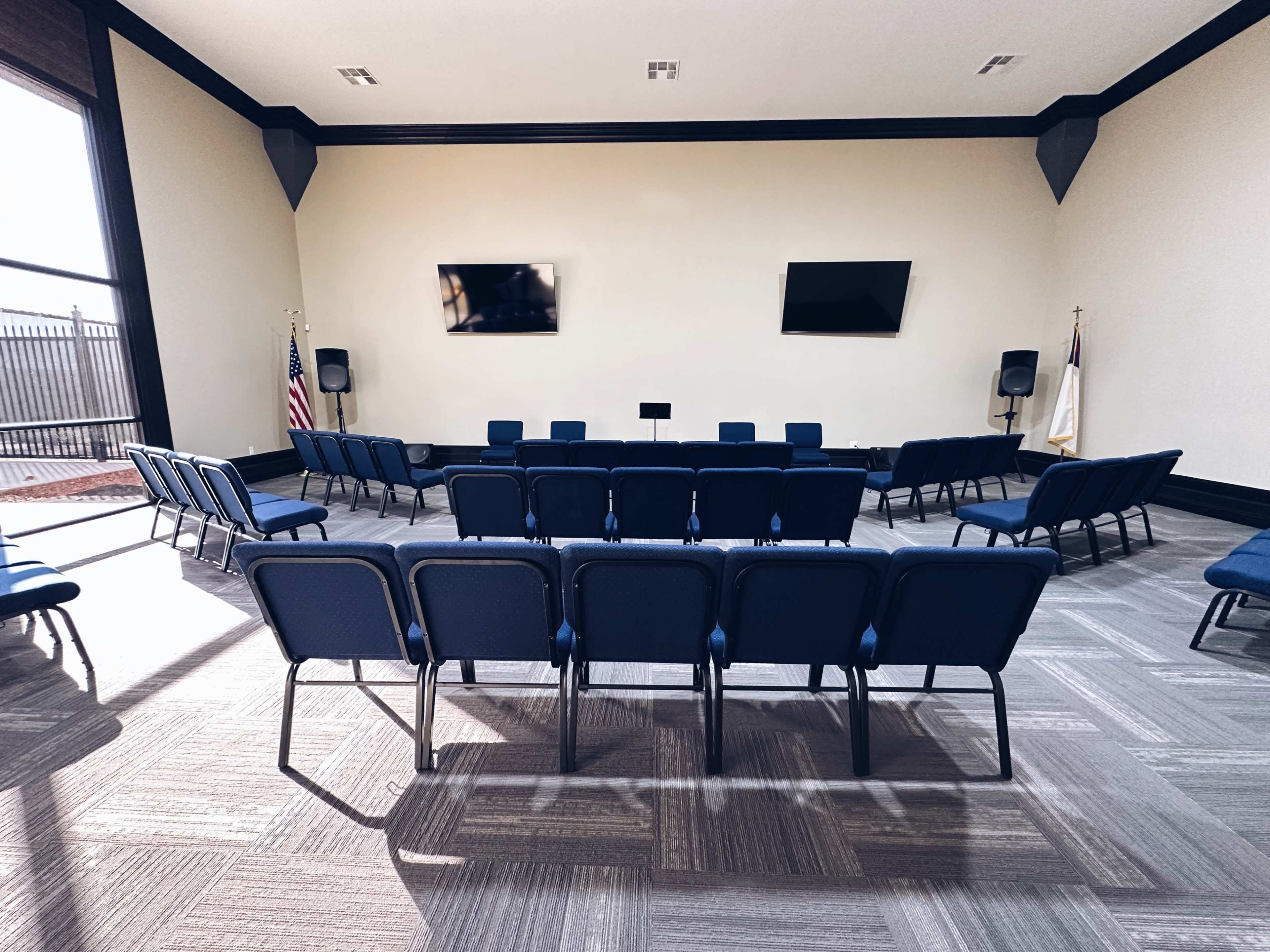 A room with rows of blue chairs arranged facing two wall-mounted screens.