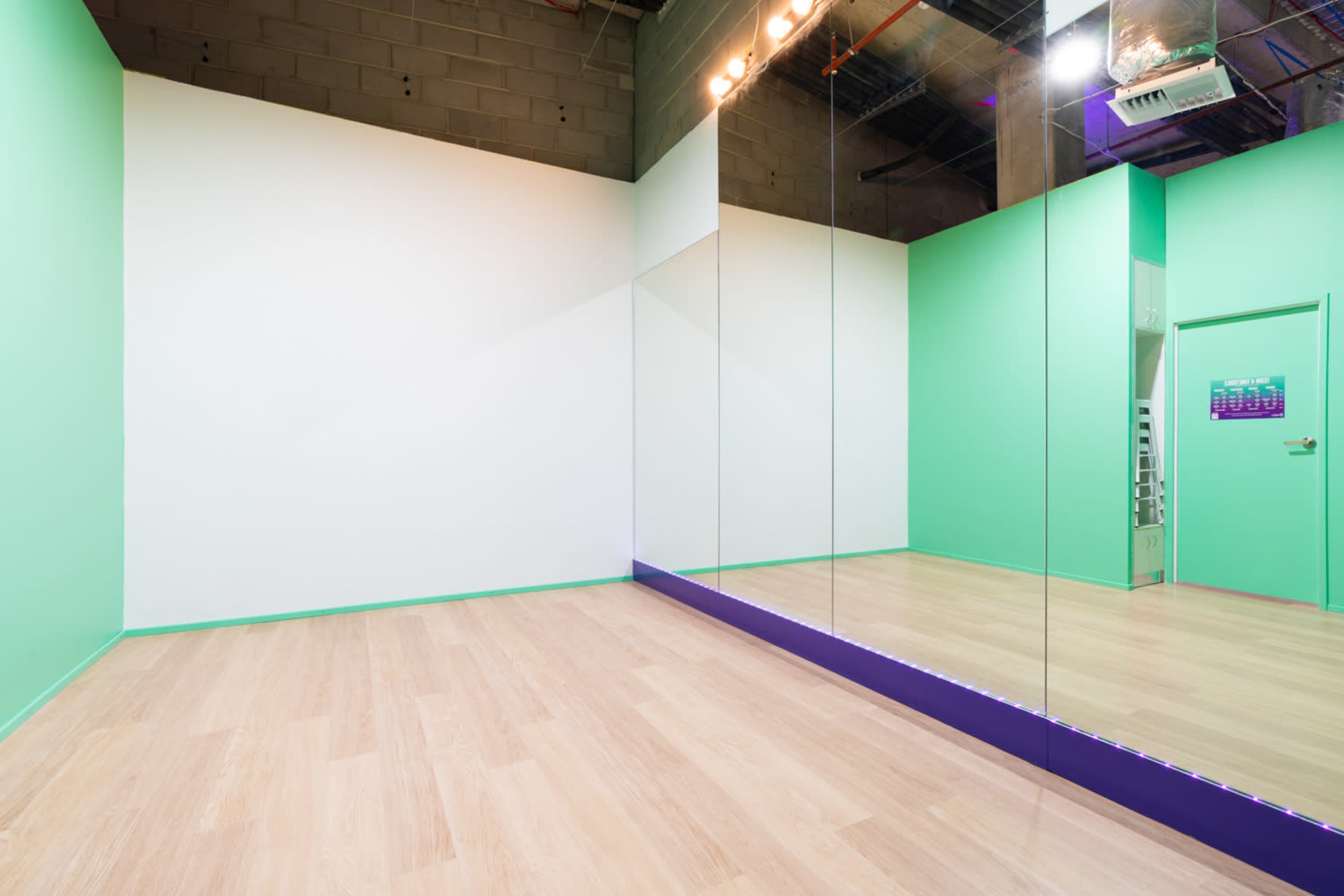 An empty room with green walls, a wooden floor, and a large mirror on one wall.