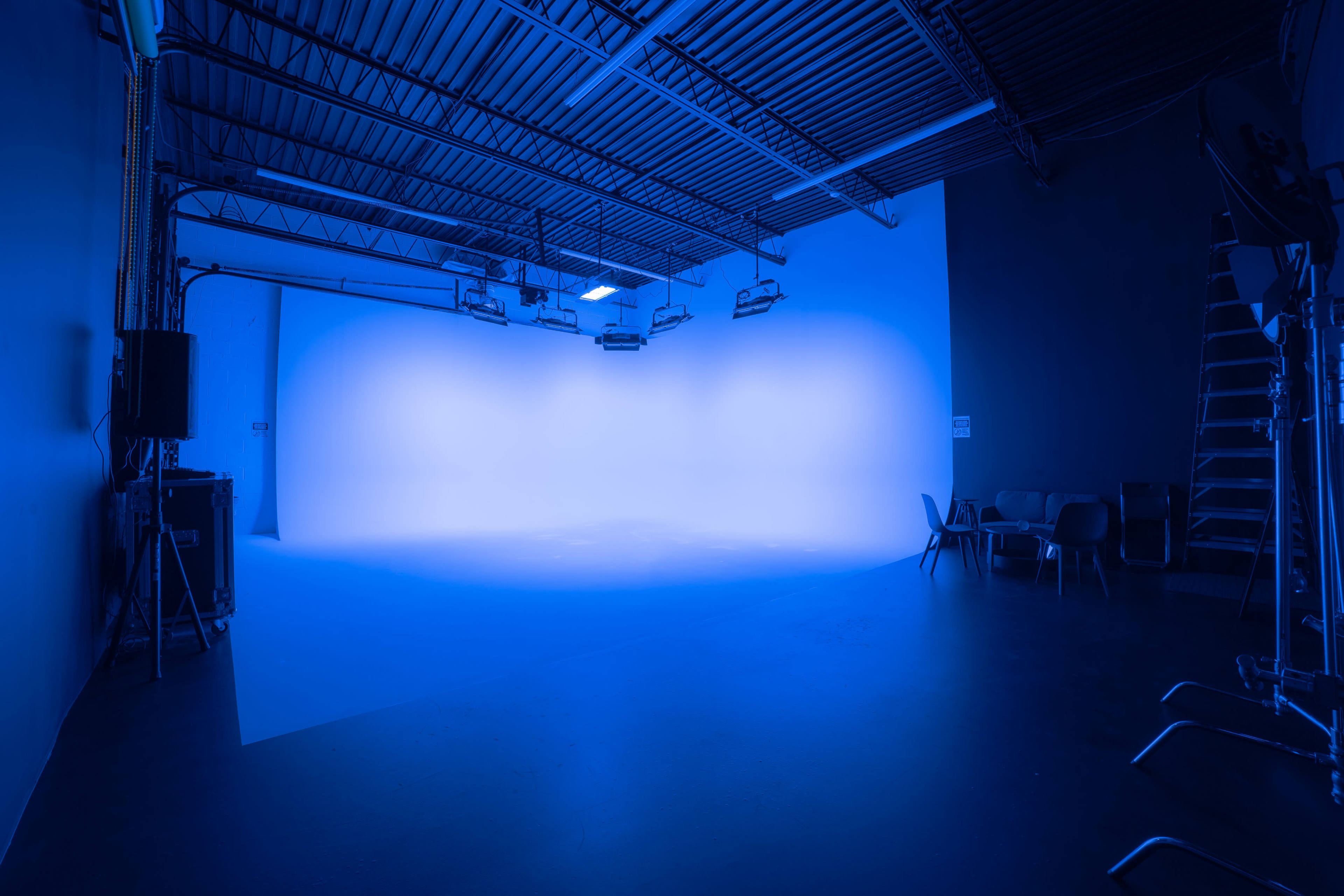 An empty studio space lit with blue lighting, featuring a smooth backdrop and minimal furniture.