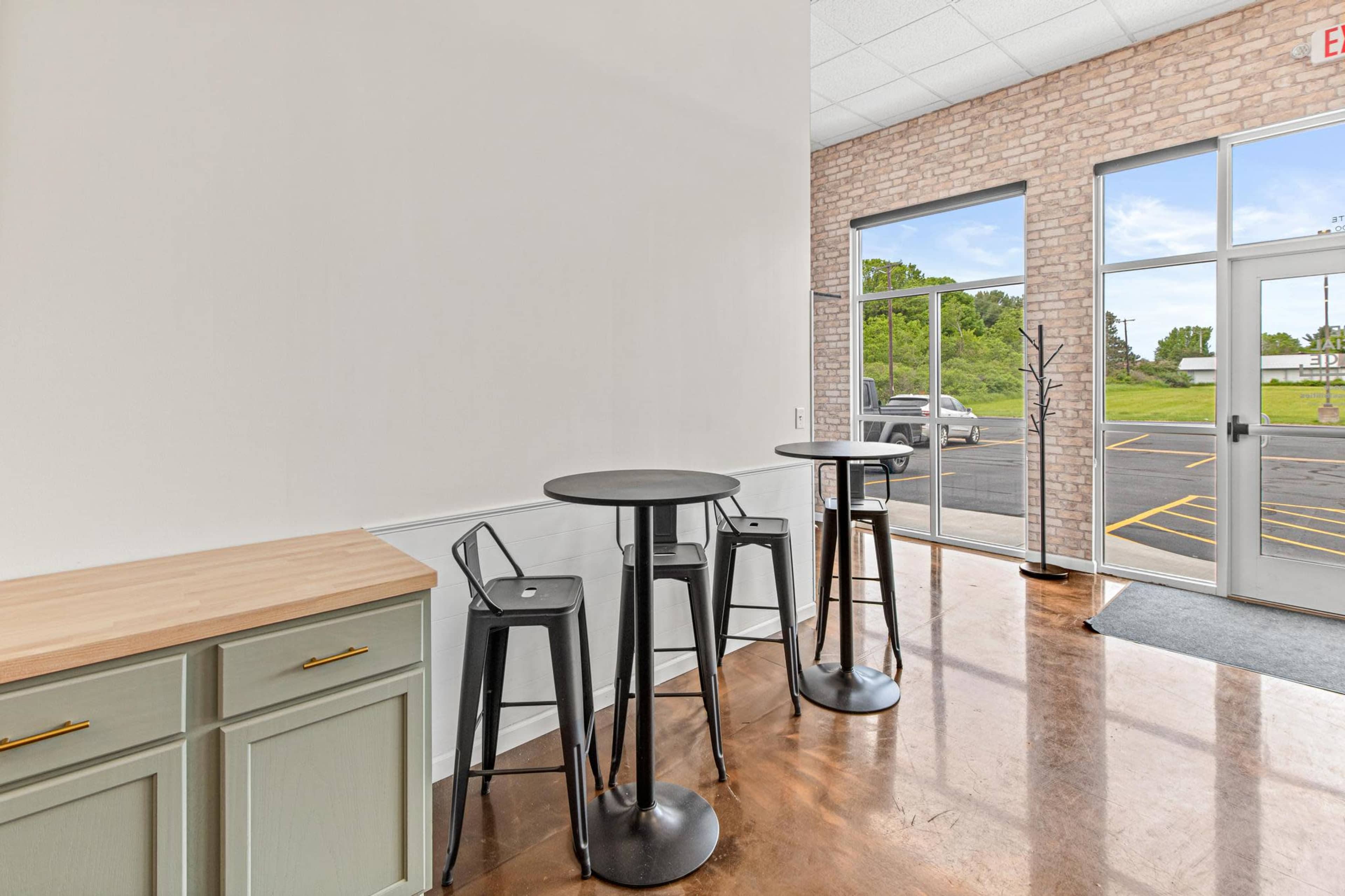 A modern interior space with two black bar tables and chairs positioned near a large window.