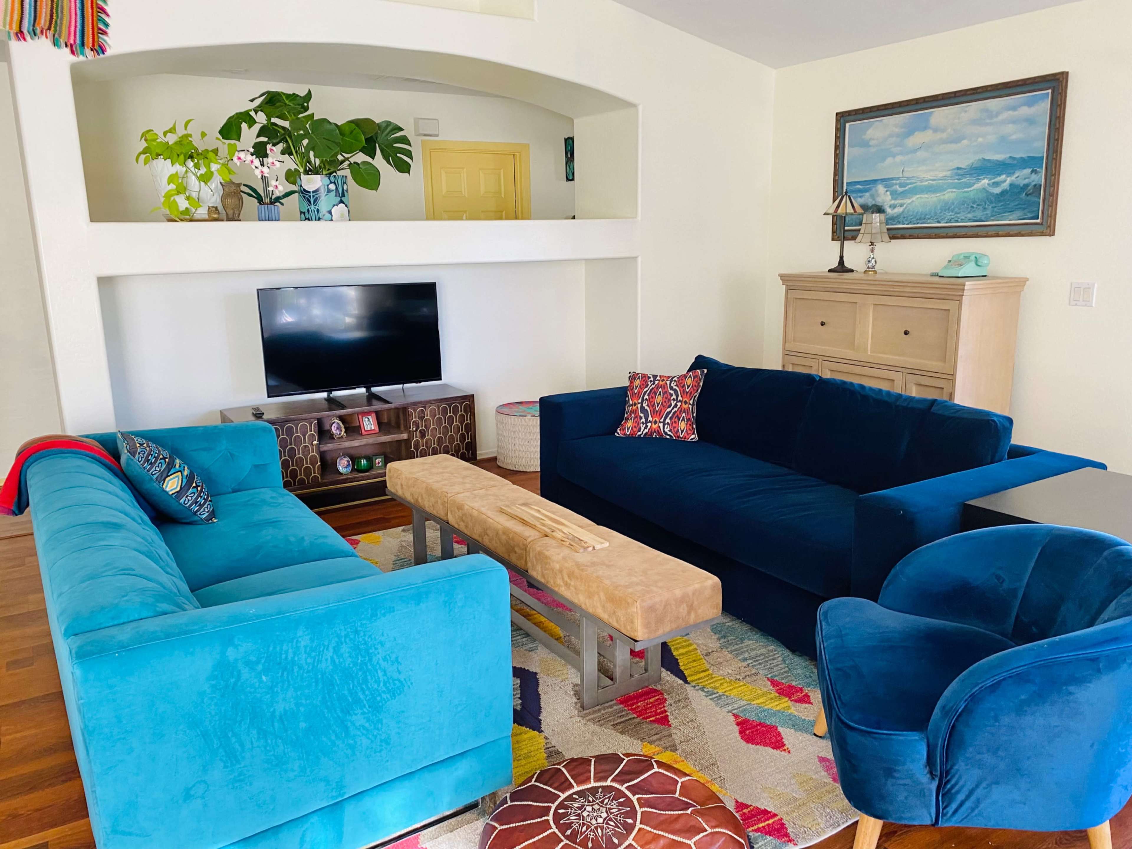 The living room features two blue sofas, a wooden coffee table, and a television on a media console against a bright, colorful rug.
