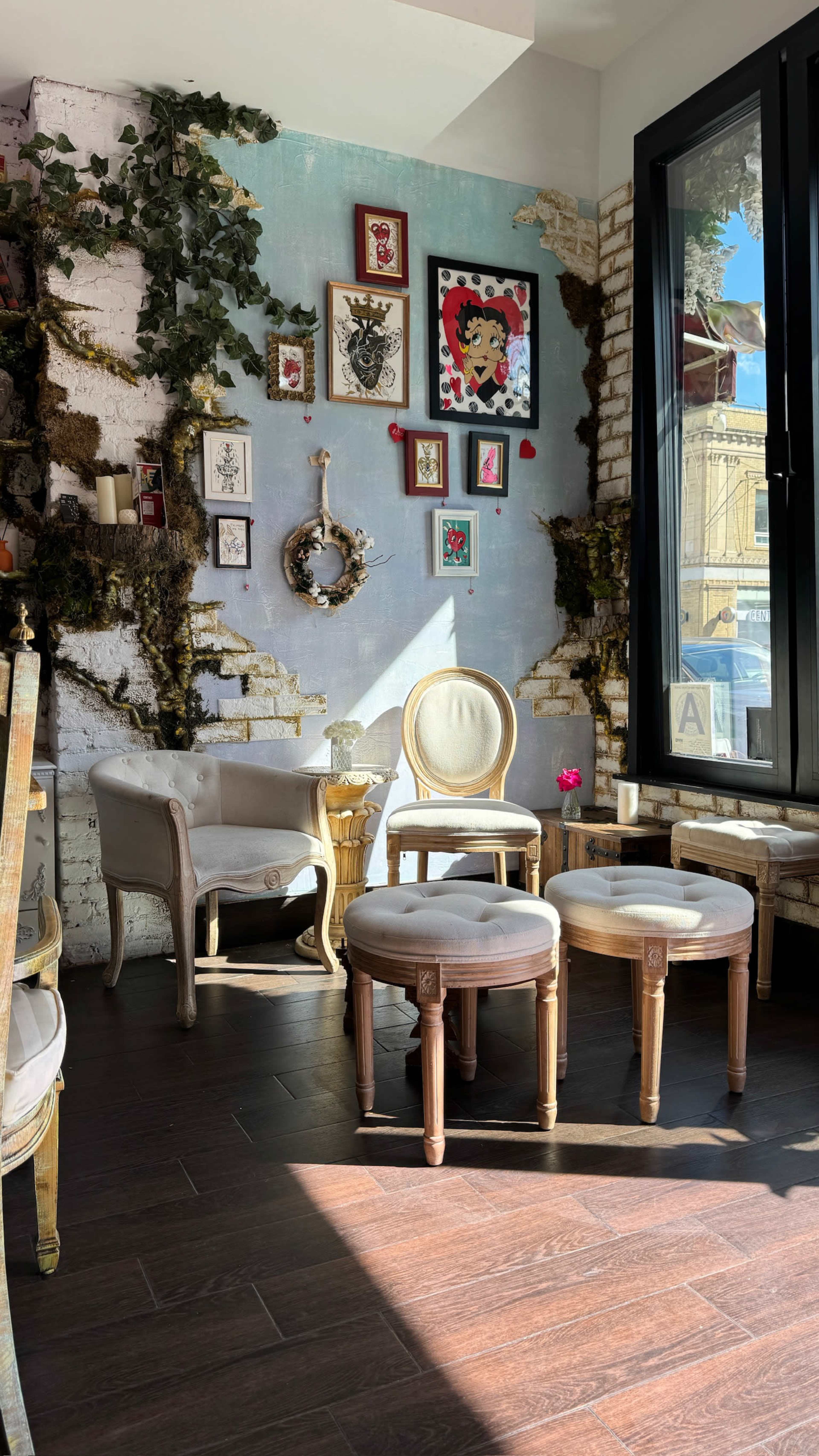 A cozy corner of a cafe features vintage furniture, a wall adorned with framed artwork, and decorative greenery climbing the walls.