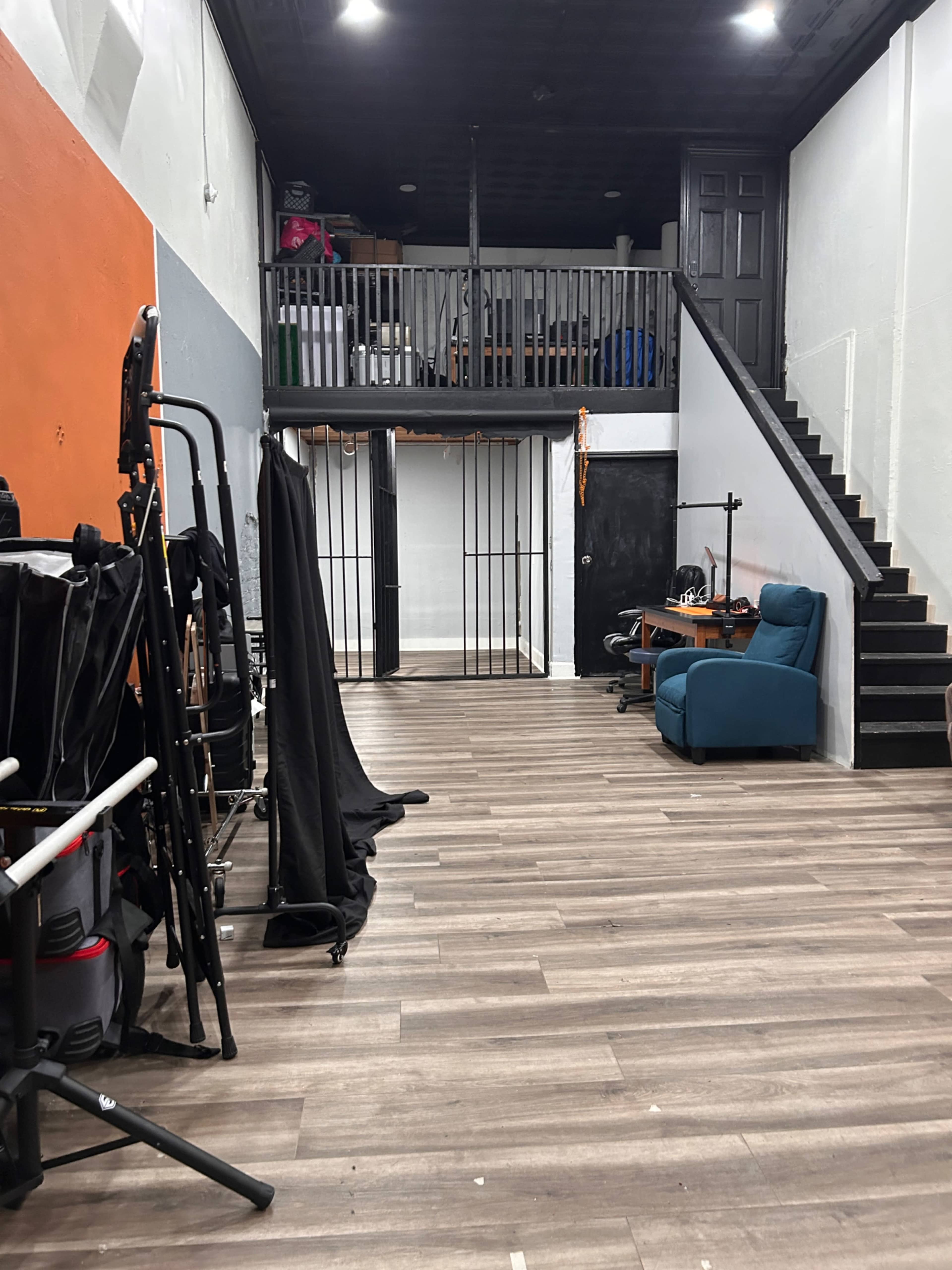 The image shows an interior space featuring a staircase, a railing overlooking a lower level, and various props including folding chairs and black drapes along one side.