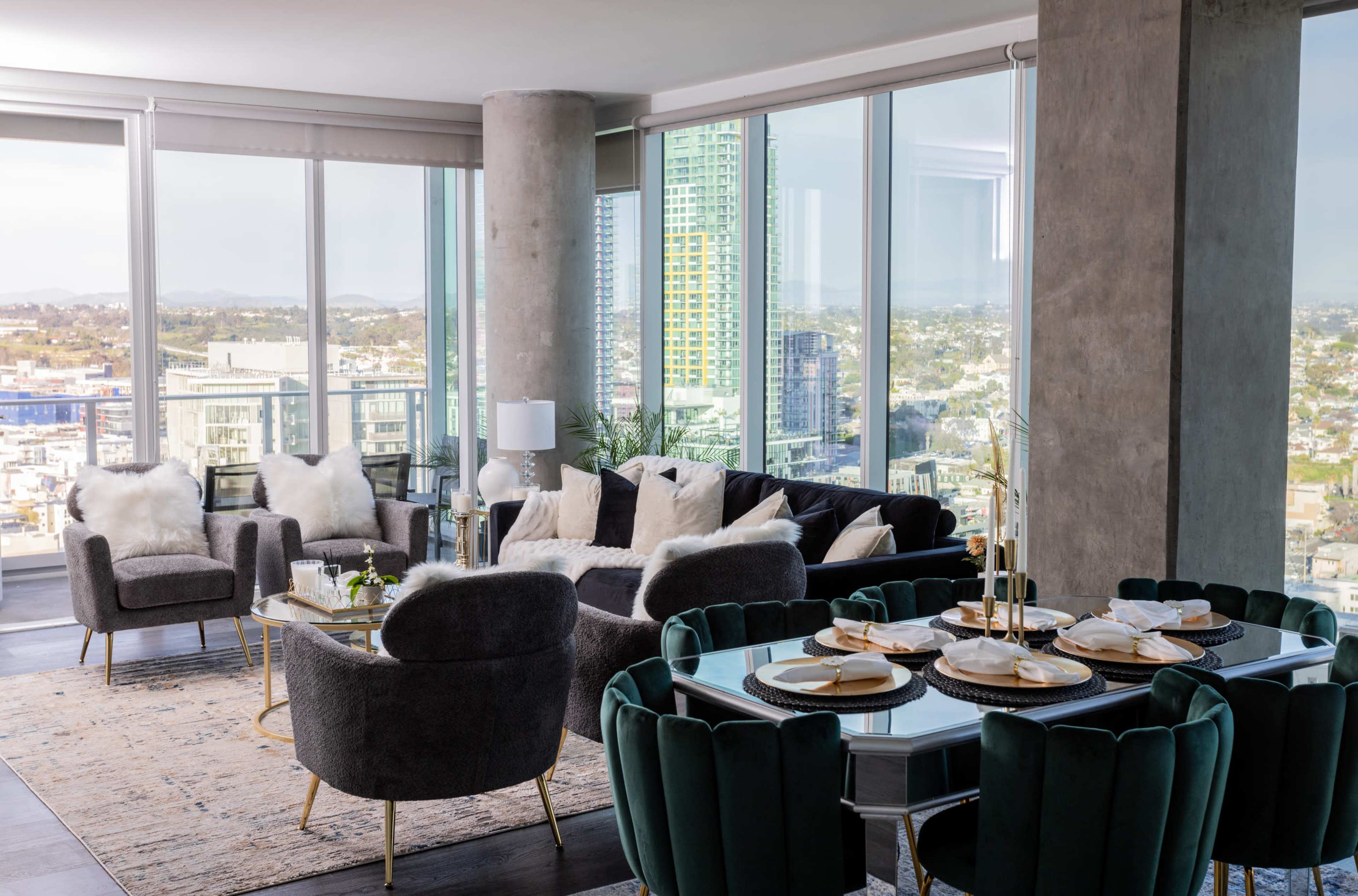 A modern living room features a seating area with plush chairs and a sofa, alongside a dining table set with tableware and a view of the city skyline through large windows.