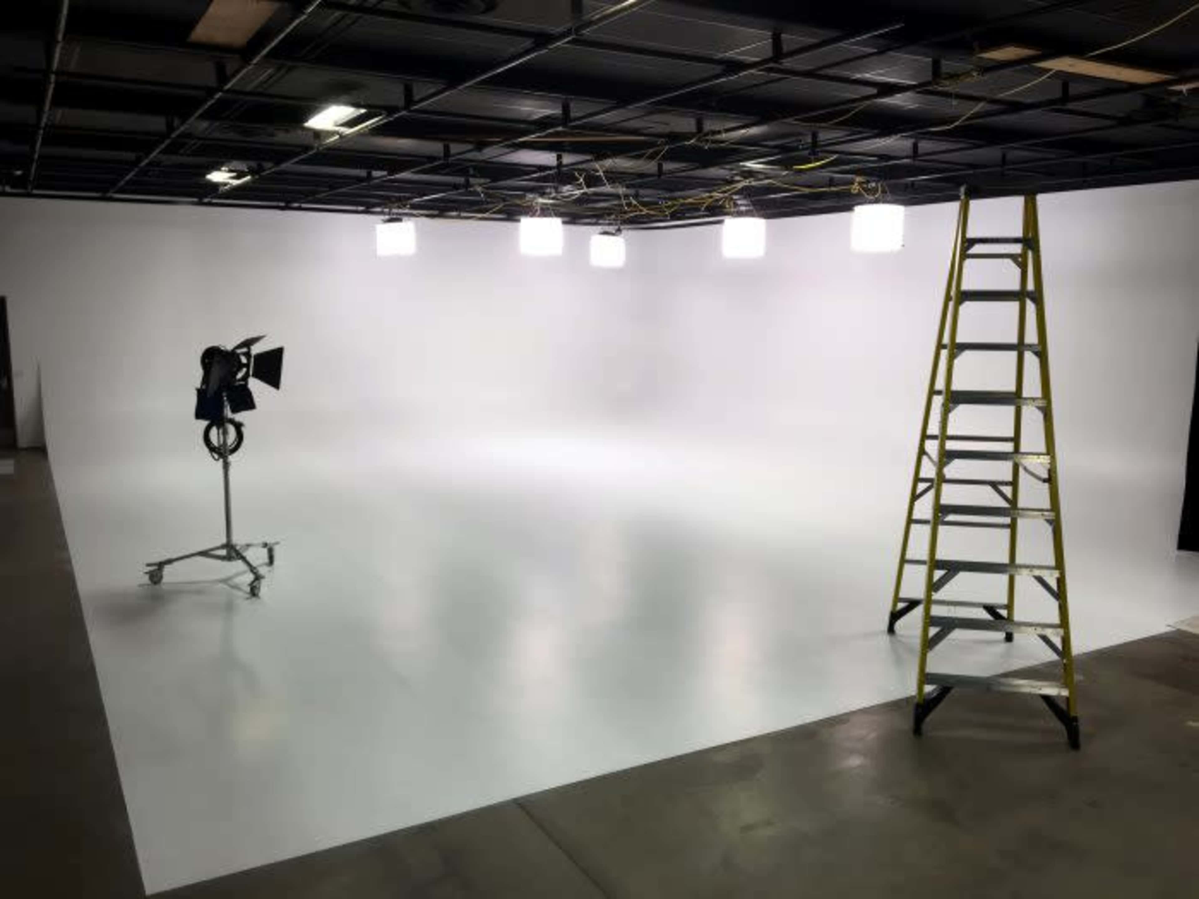 A sparse photography studio with a white backdrop, a ladder, and studio lights on stands.