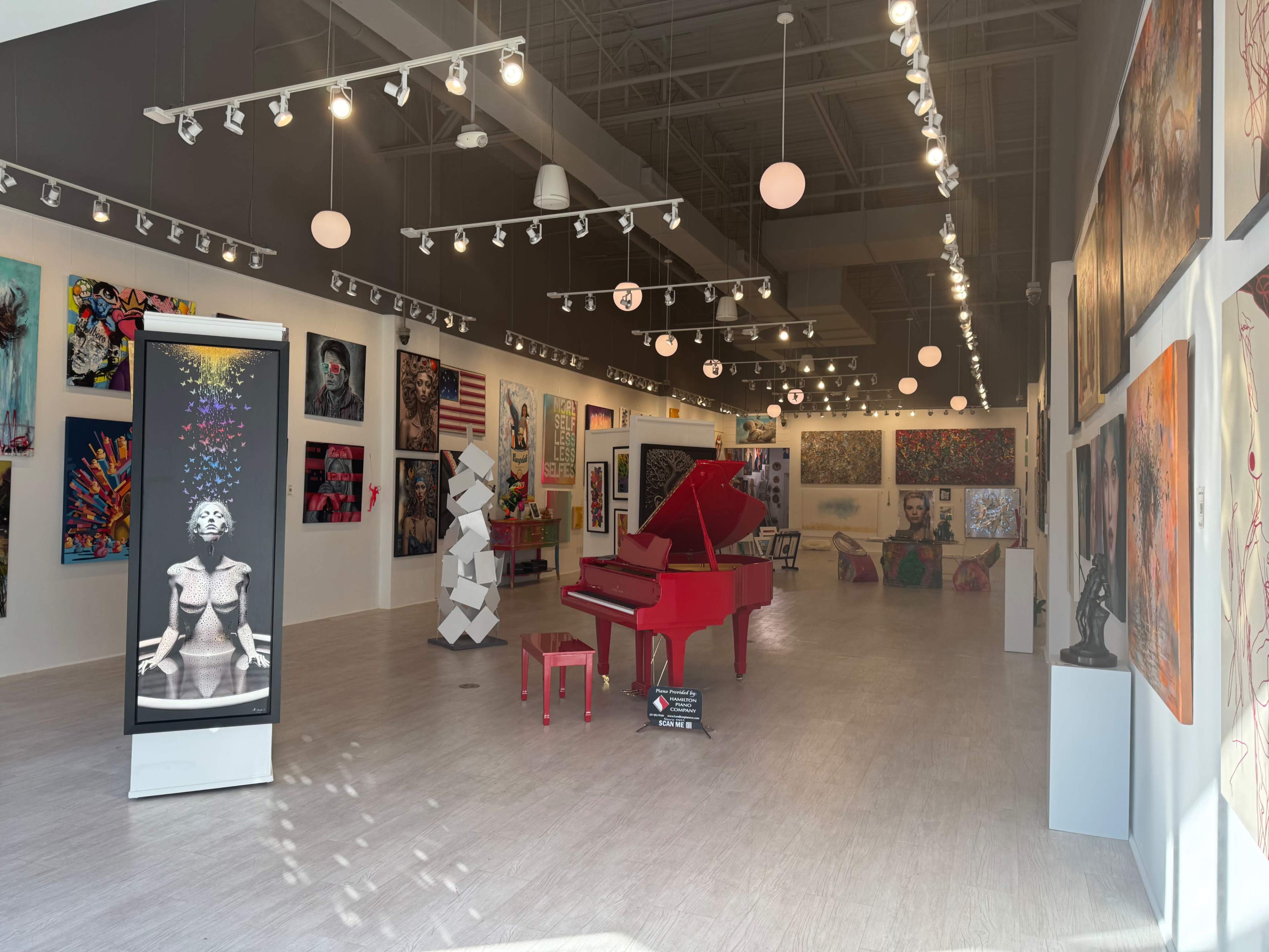 The image shows an art gallery featuring various artworks on the walls, a red grand piano in the center, and a modern sculpture in the foreground.