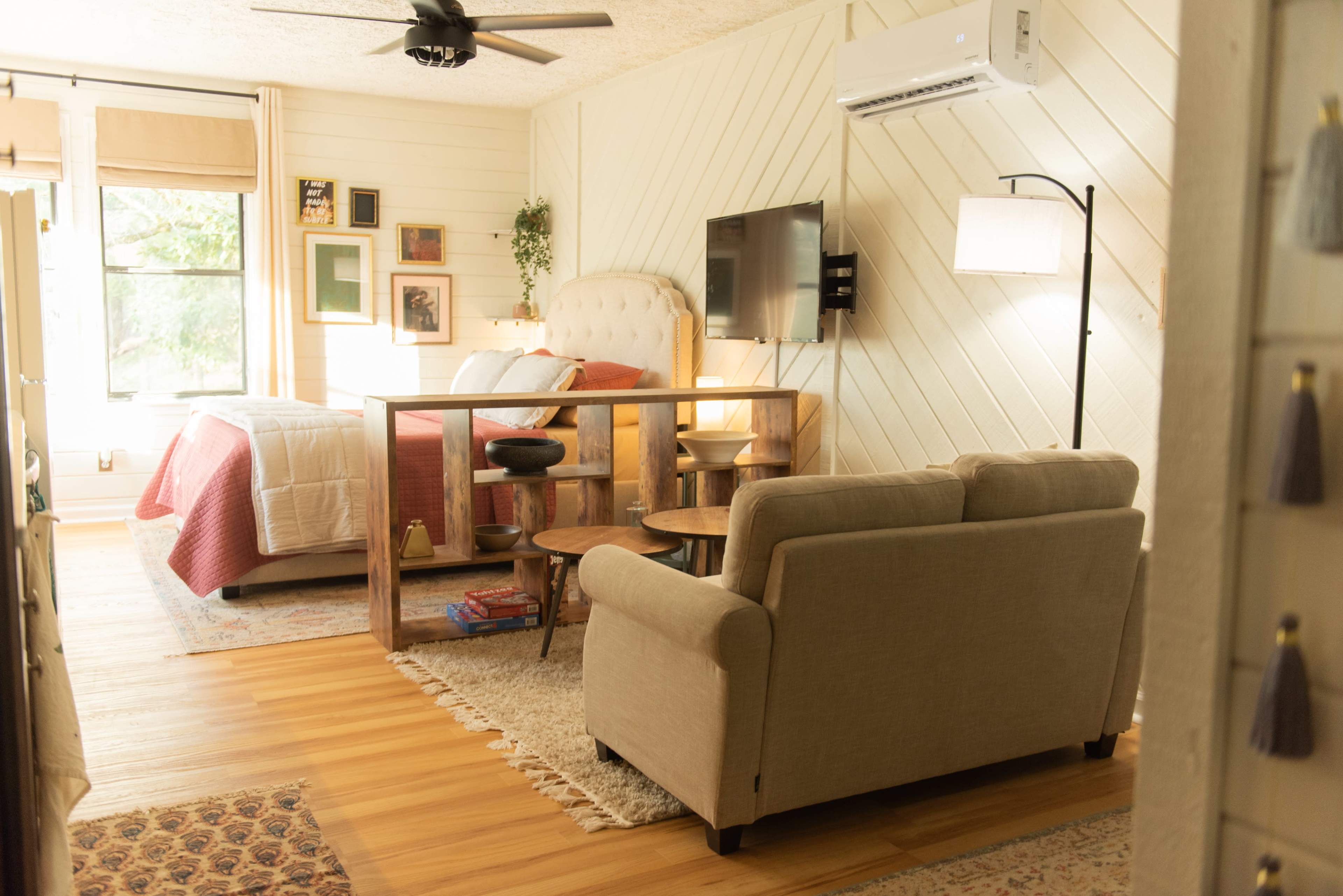 A cozy bedroom with a wooden bed frame, a small seating area with a sofa, and a television mounted on the wall.