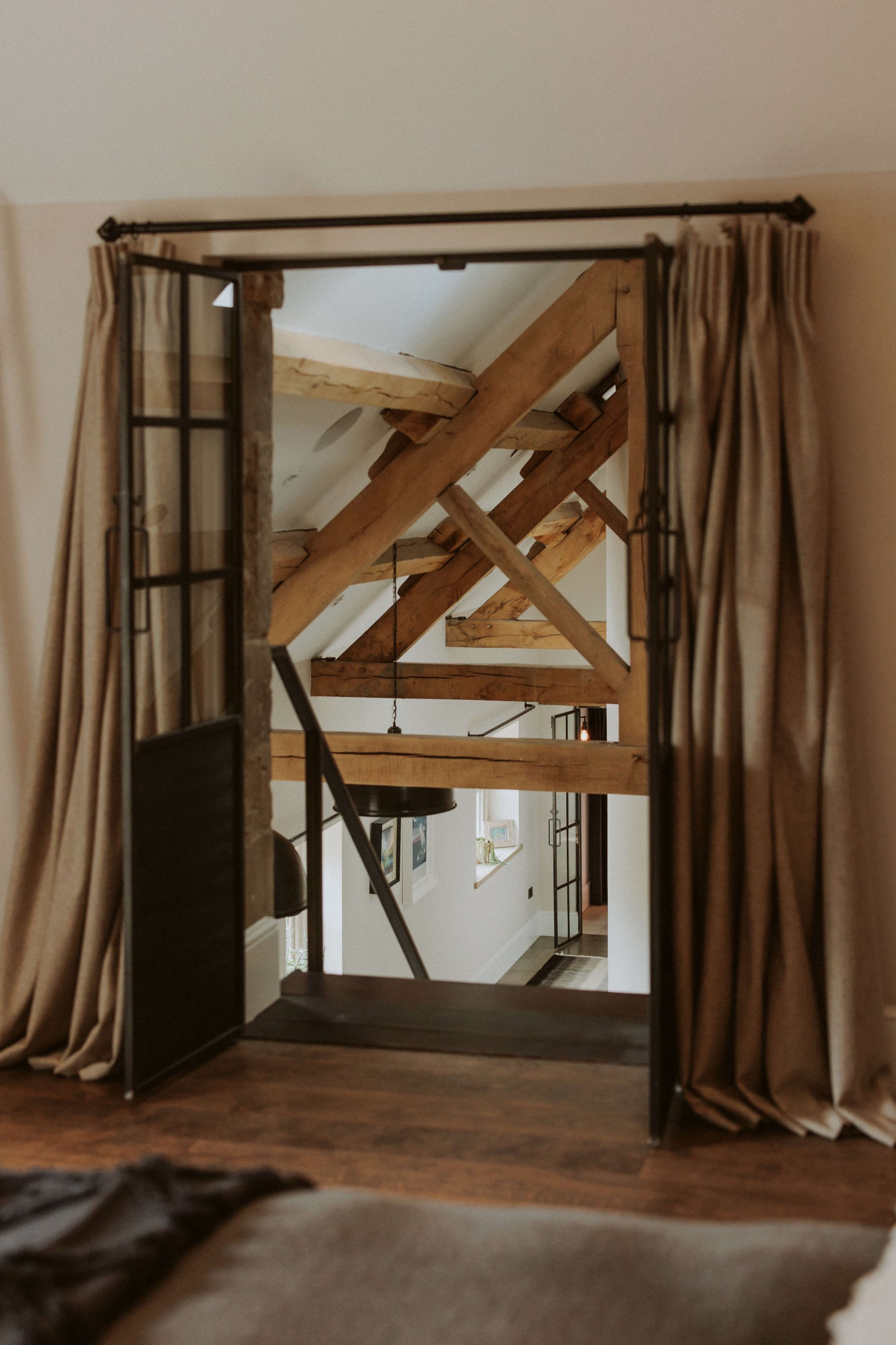 A doorway with open curtains reveals a room featuring exposed wooden beams and large windows.