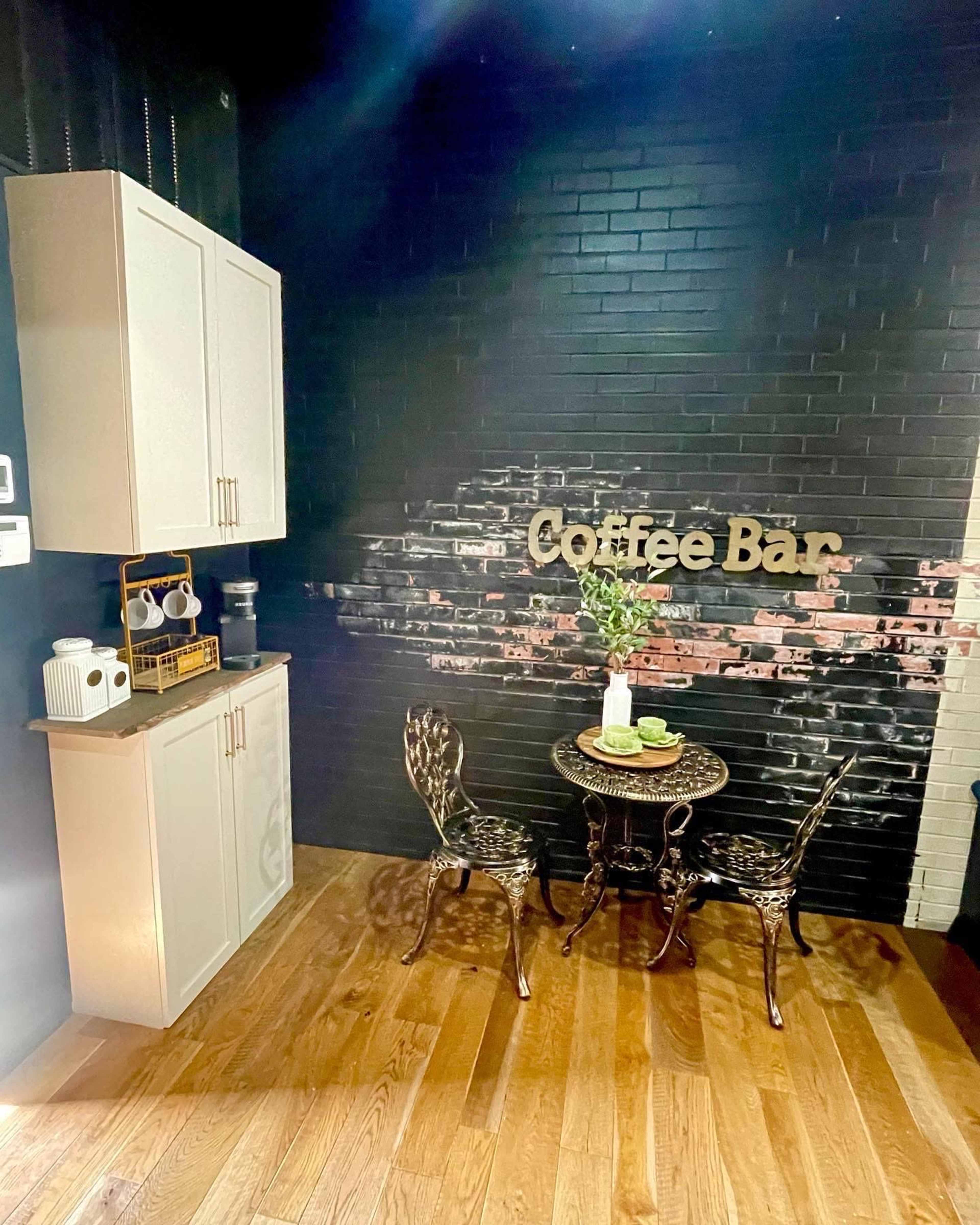 The scene features a small coffee bar setup with a table and two chairs against a black-brick wall, decorated with the words "Coffee Bar."