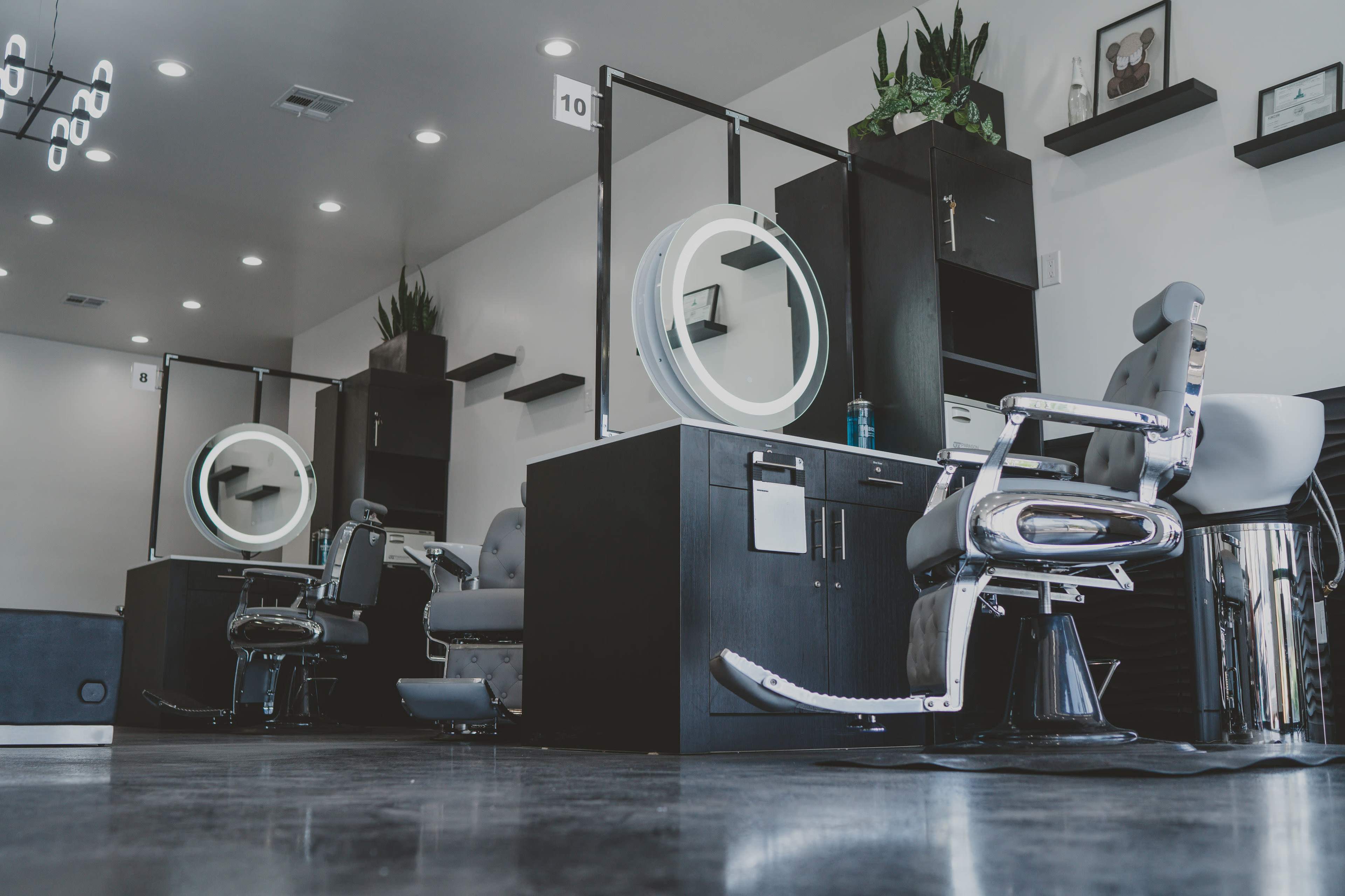 A modern hair salon interior with two styling stations featuring large round mirrors, black cabinetry, and sleek silver salon chairs.