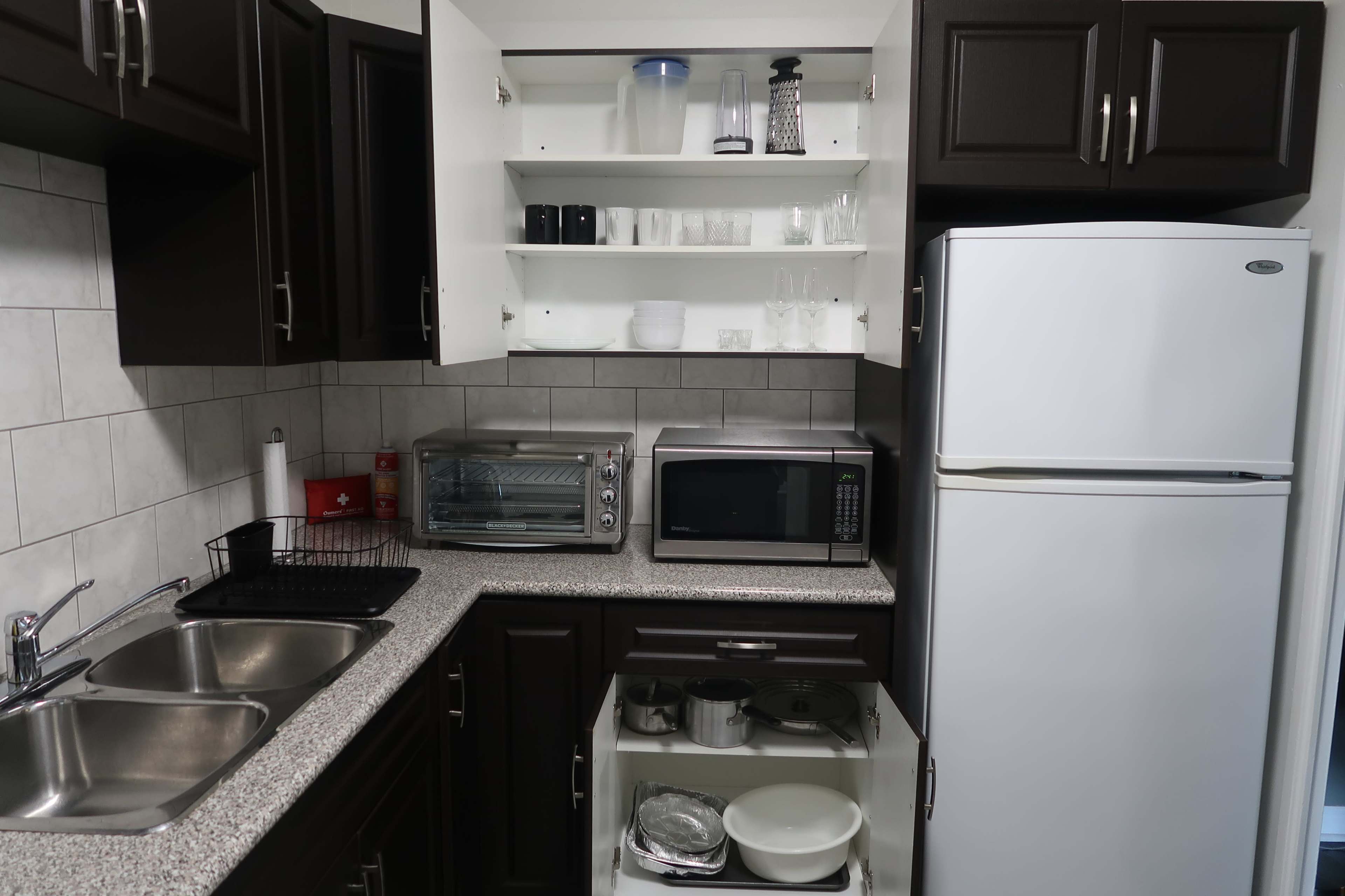 A modern kitchen with dark cabinets, a countertop, a sink, an oven, a microwave, a refrigerator, and neatly arranged dishware on open shelves.