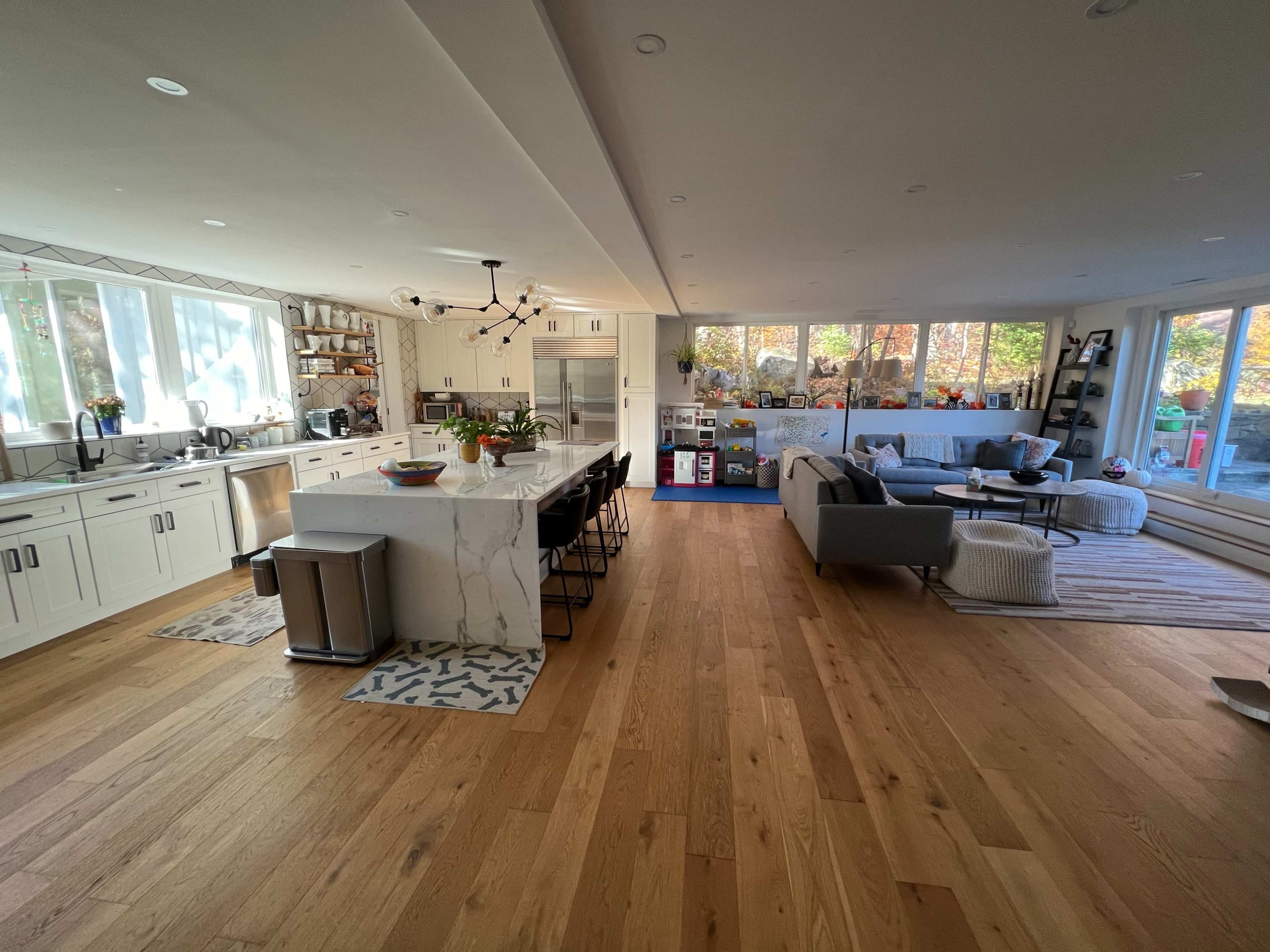 A spacious kitchen and living area feature a large island with bar seats, modern appliances, and large windows that allow natural light to fill the space.