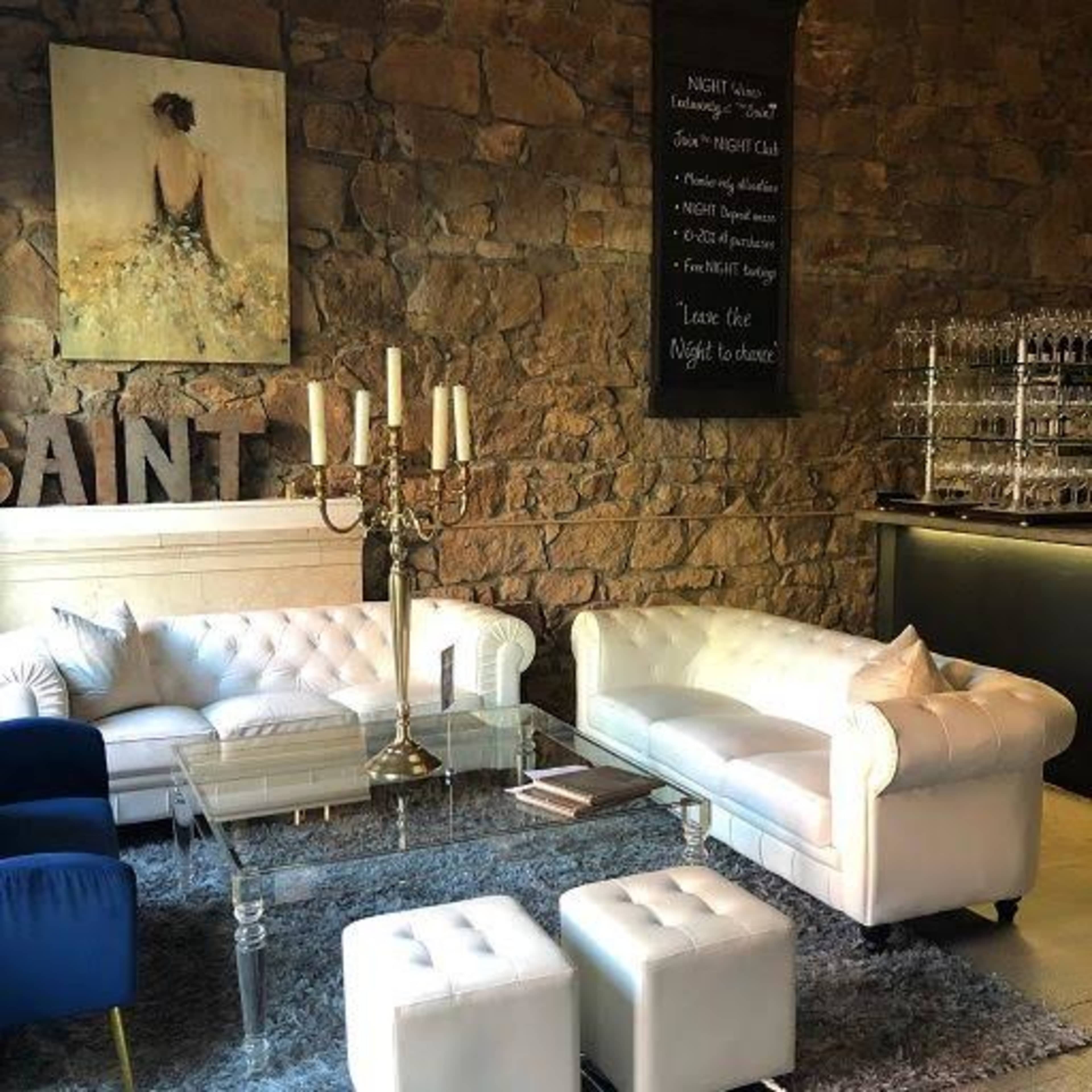 A stylish lounge area with a white leather couch, a glass coffee table, and a large painting on a stone wall.