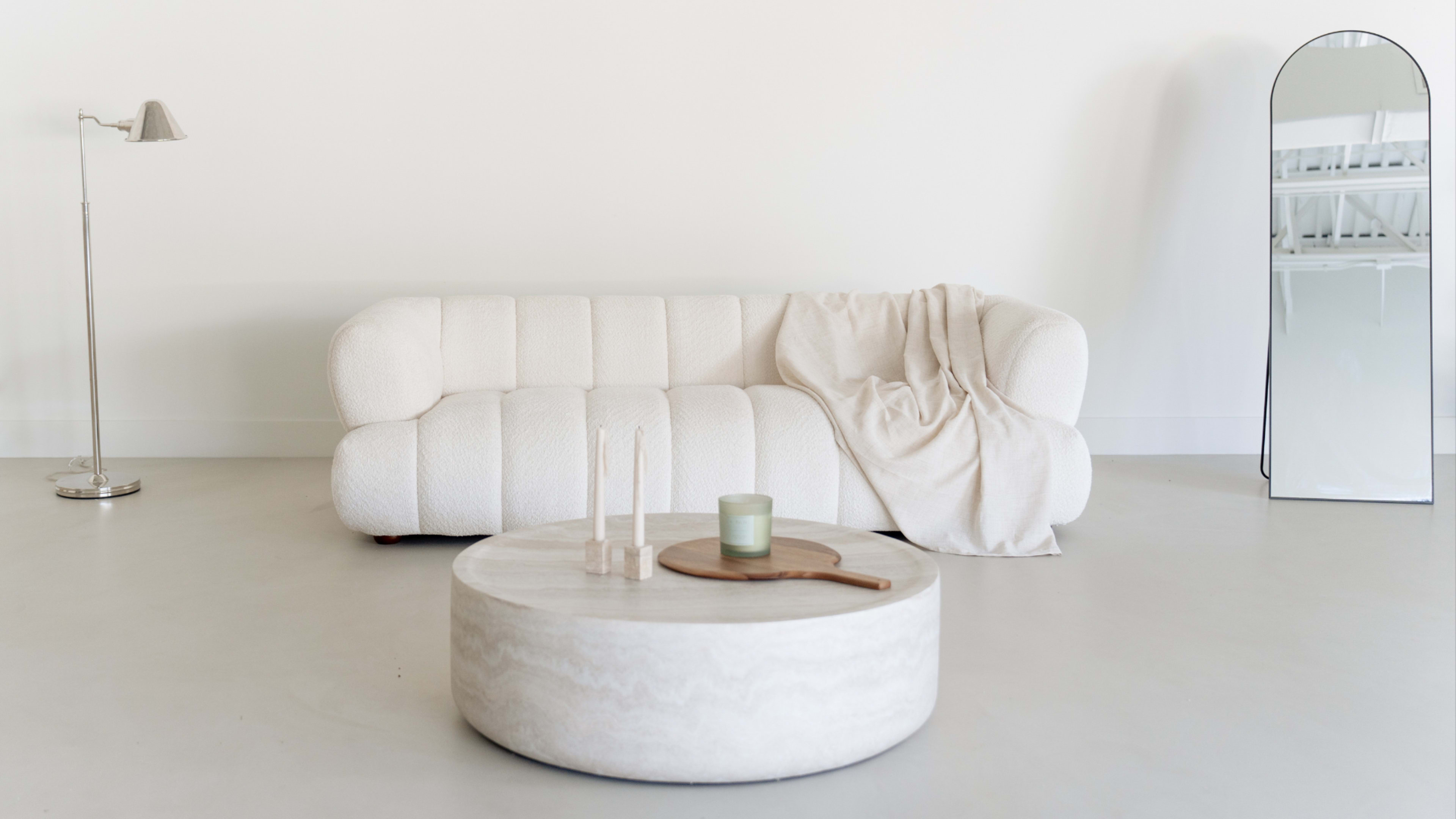 The image features a minimalist living room with a white, textured sofa, a round coffee table, and a standing lamp.