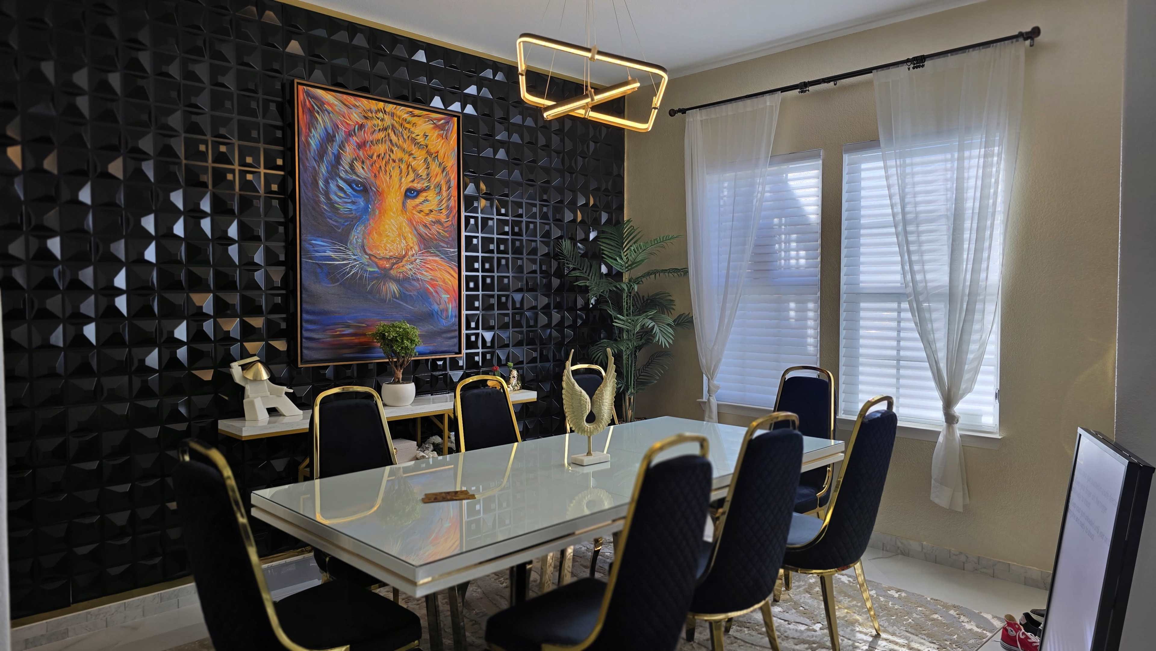 The image shows a stylish dining area featuring a glass table surrounded by eight upholstered chairs, a vibrant tiger painting on the textured black wall, and a decorative plant near the window.