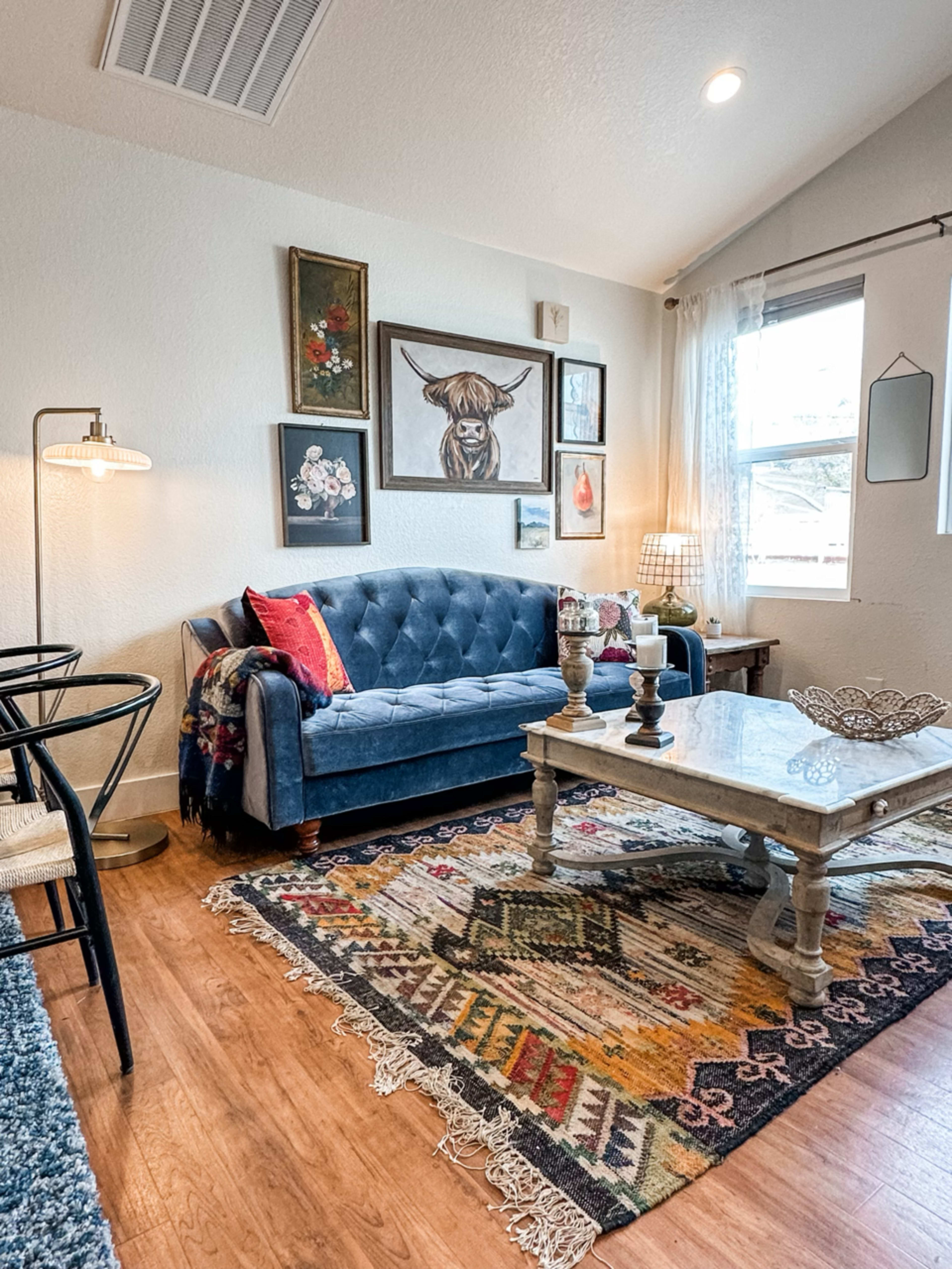 A cozy living room featuring a blue tufted sofa, a coffee table, and a colorful patterned rug.