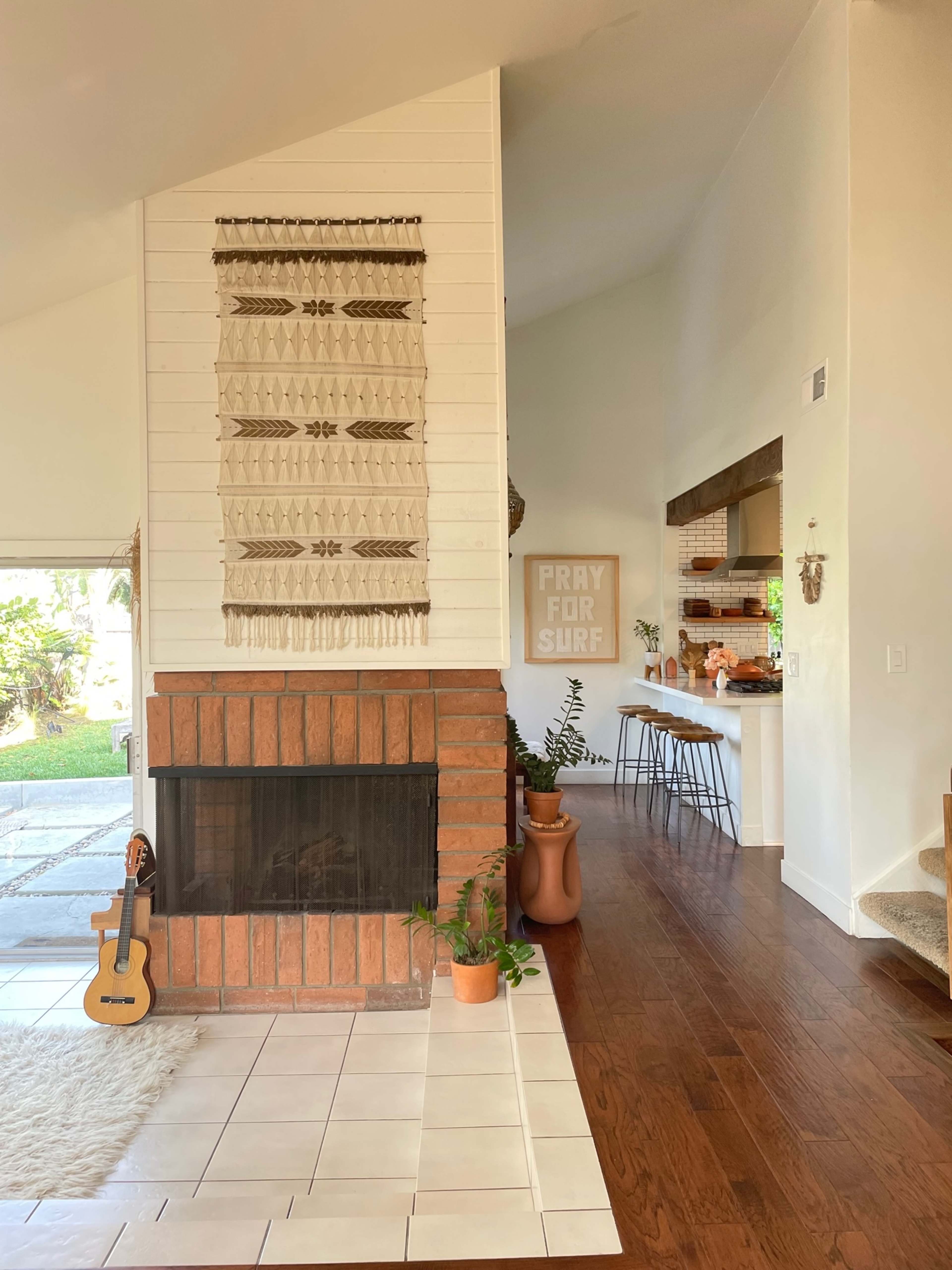 The image shows a bright living space with a fireplace, wall art, and a view of a kitchen and dining area beyond.