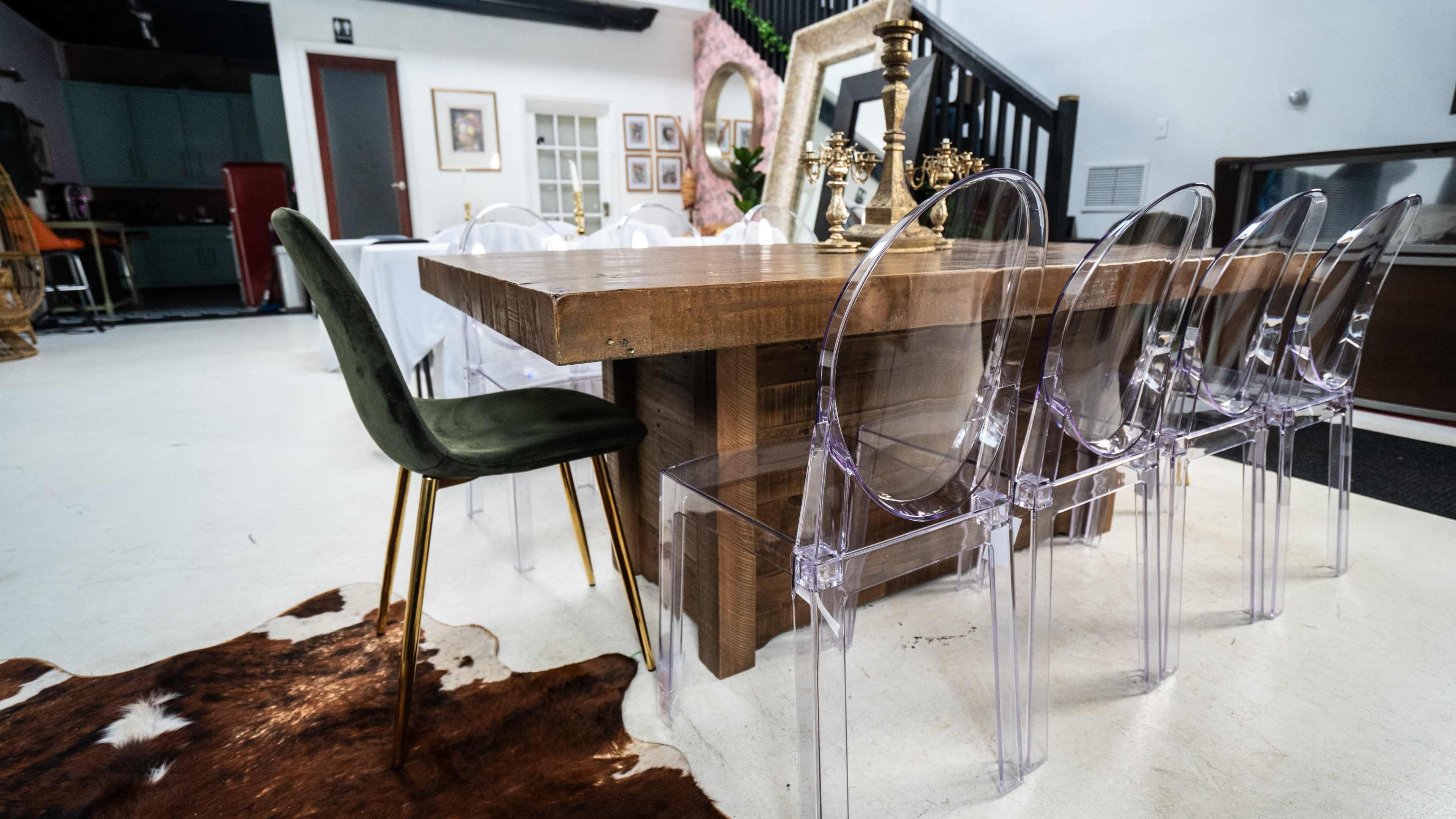 A wooden dining table is surrounded by transparent acrylic chairs on a cowhide rug in a modern interior space.