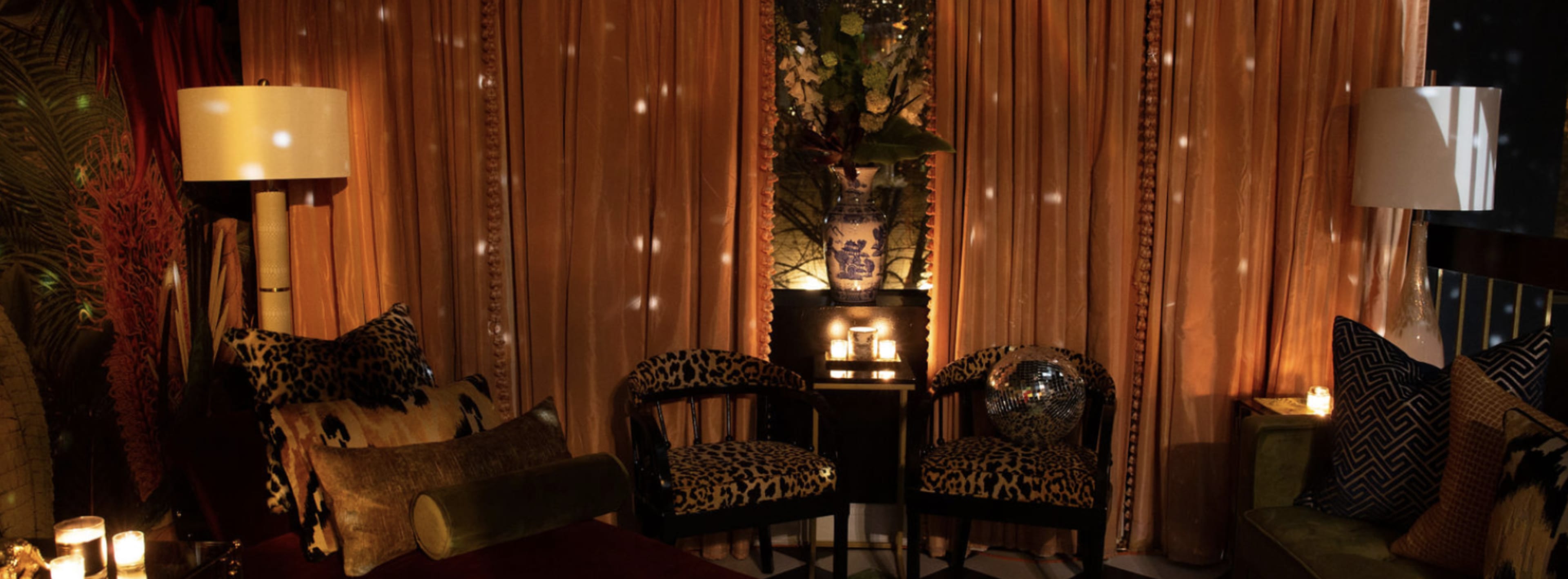 A cozy seating area with two leopard-print chairs, warm lighting from lamps and candles, and decorative curtains.