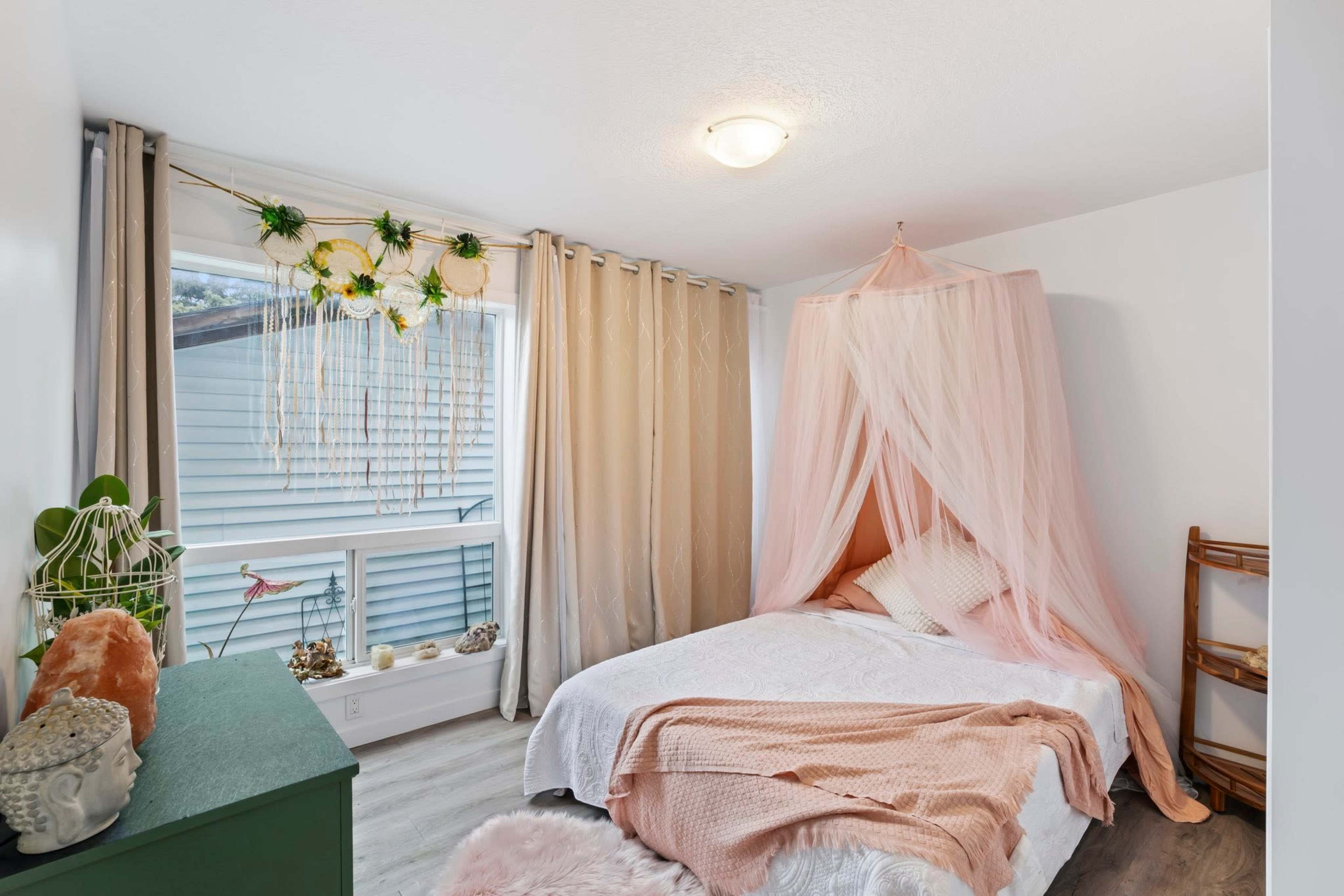 The image shows a cozy bedroom with a bed draped in light fabric, a window with sheer curtains, and a green dresser.