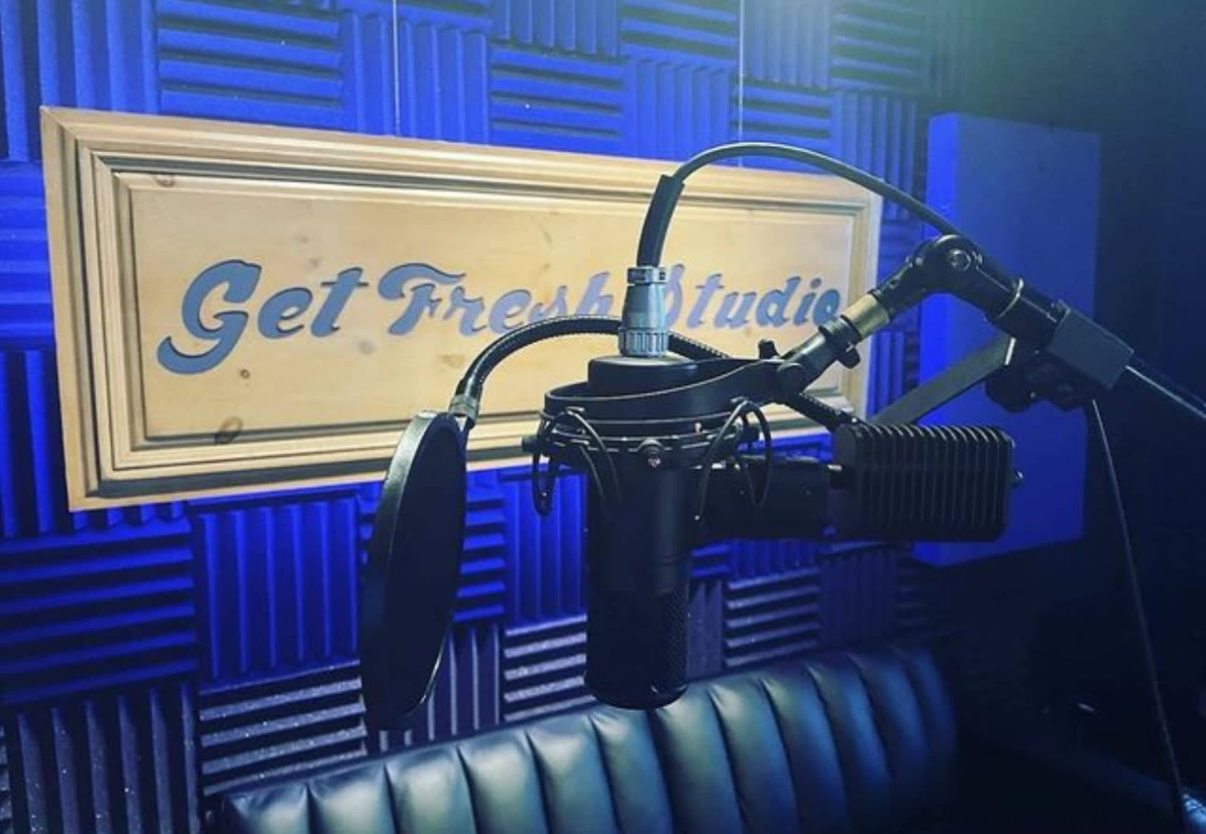 A microphone is positioned in front of a wooden sign that reads "Get Fresh Studio," with sound-absorbing panels in the background.